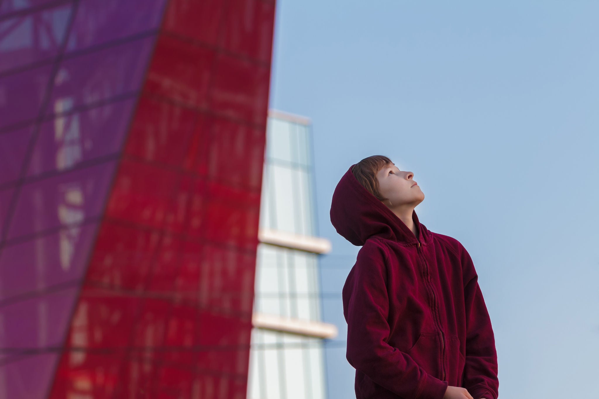 Urban portrait of teenager is wearing maroon hooded sweatshirt  at modern glass skyscraper city background