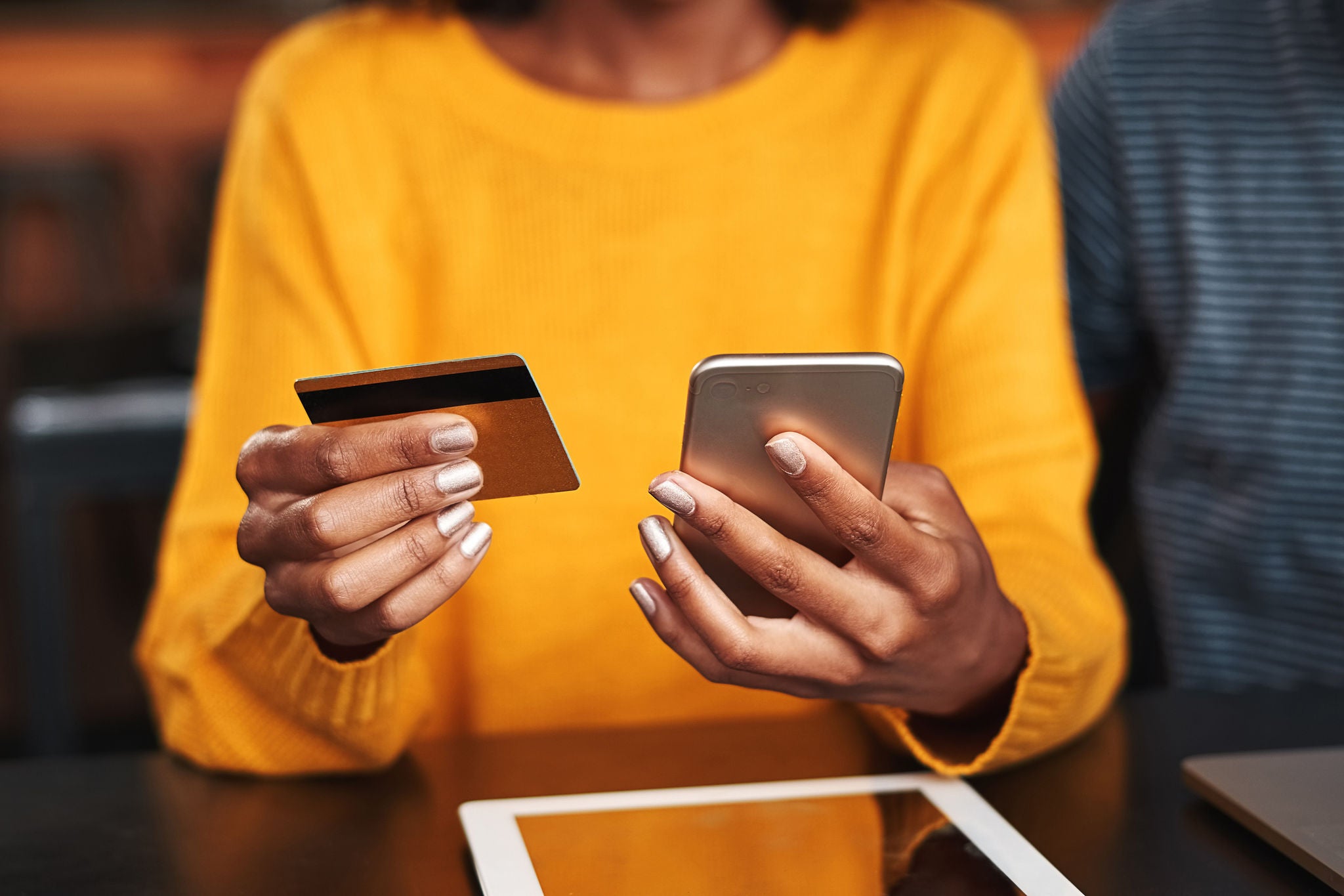 Close-up of a young woman in cafeteria using mobile phone and credit card for shopping online