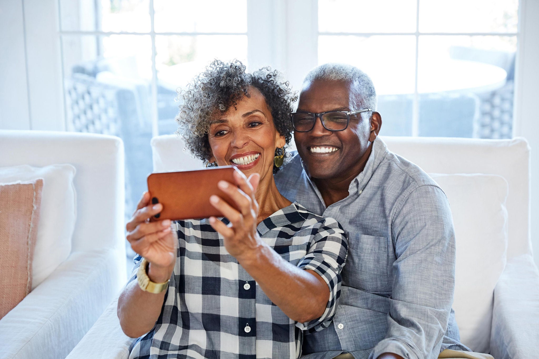 Happy retired mature African American couple at home in their living room taking a selfie with a smart phone