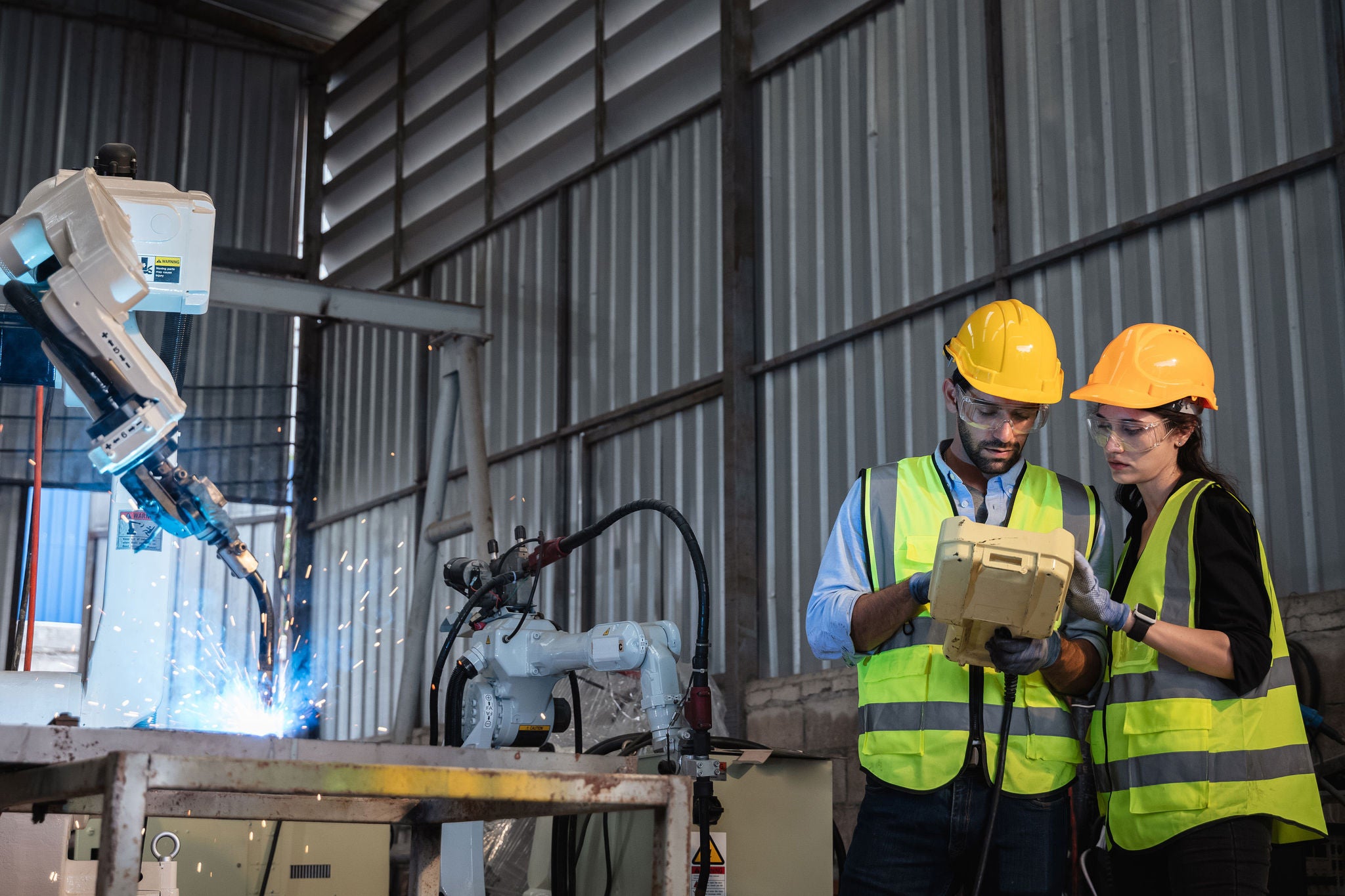 Industrial engineers are controlling the automated robot arms machine welding steel welding robots in industrial manufacturing factory.