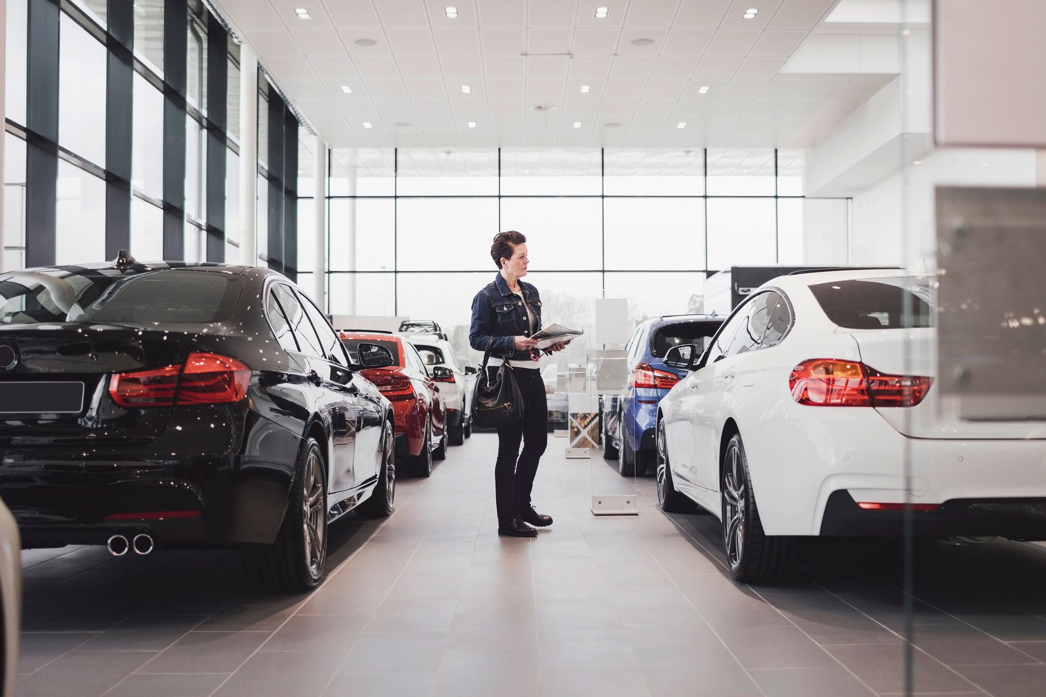 Senior woman holding documents and looking at cars in showroom