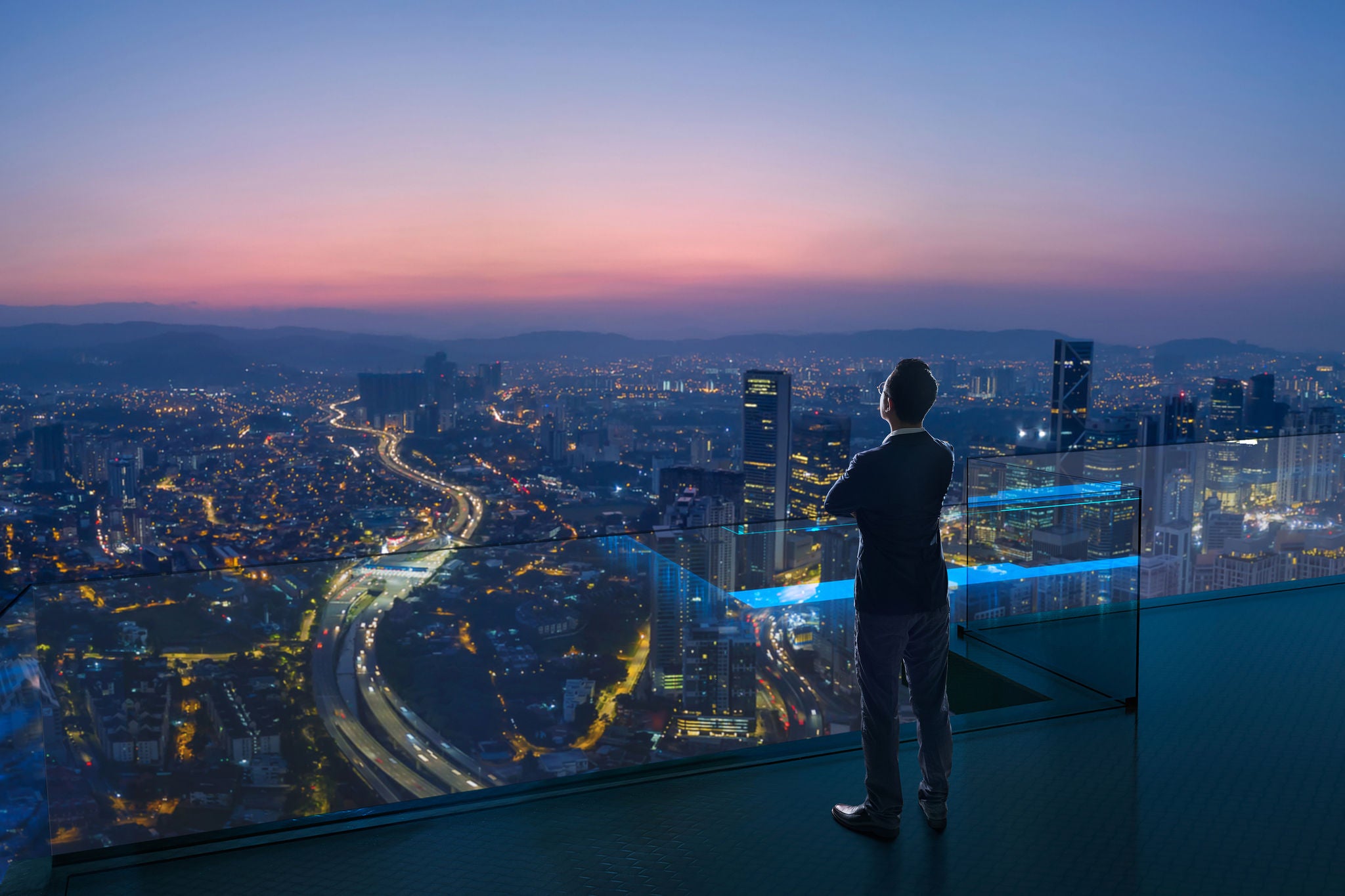 Businessman standing on open roof top balcony watching city night view