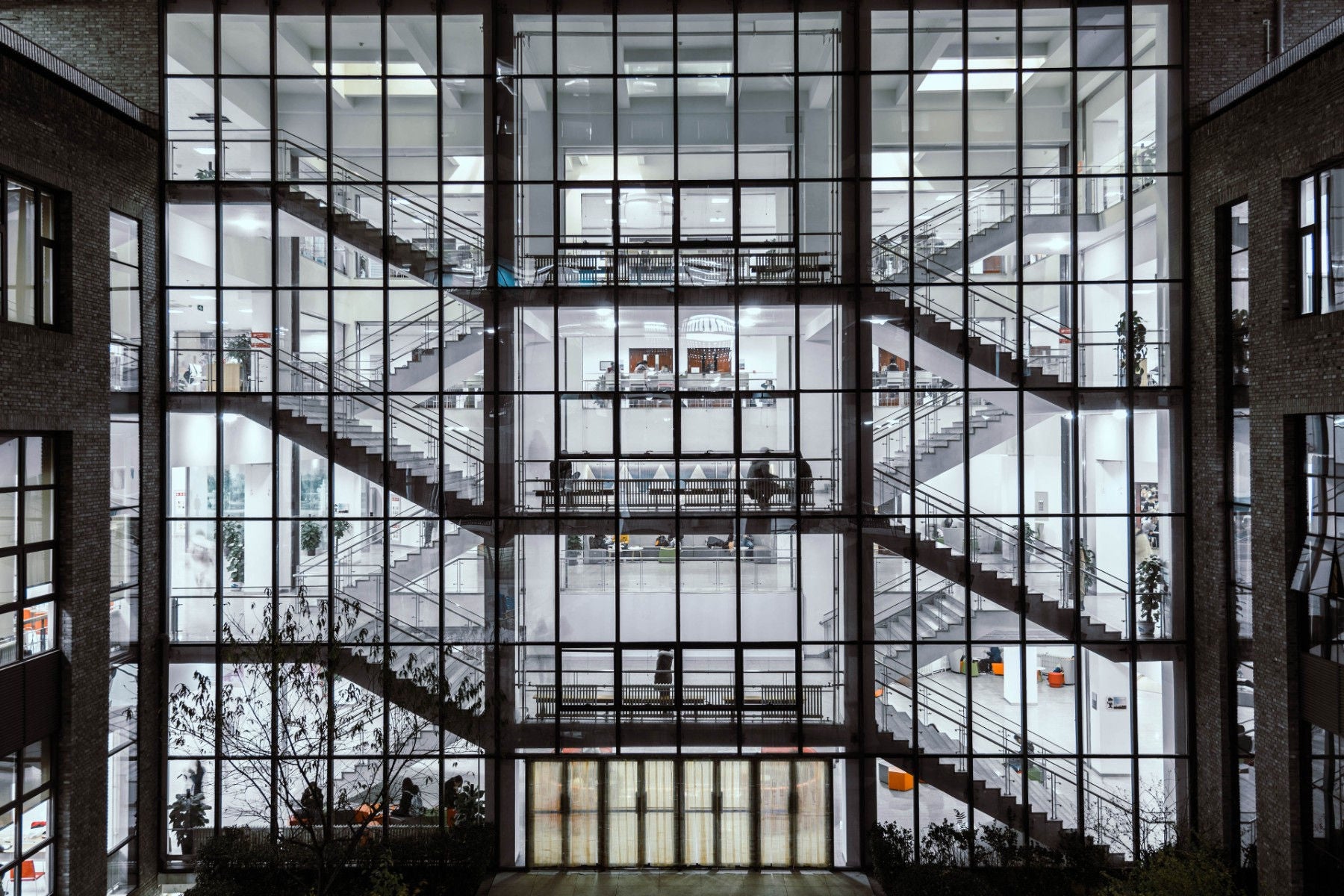 Edificio moderno con ventanales amplios que dejan ver escaleras, oficinas y personas en su interior.