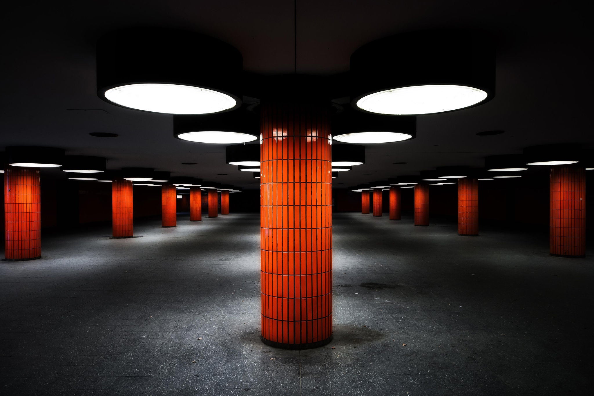 Orange tiled columns and big round lights in subway station.