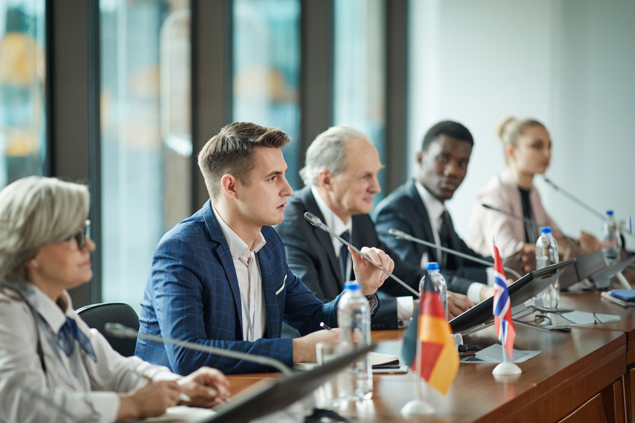 Young businessman sitting at the table and speaking the speech during debates with other political leaders