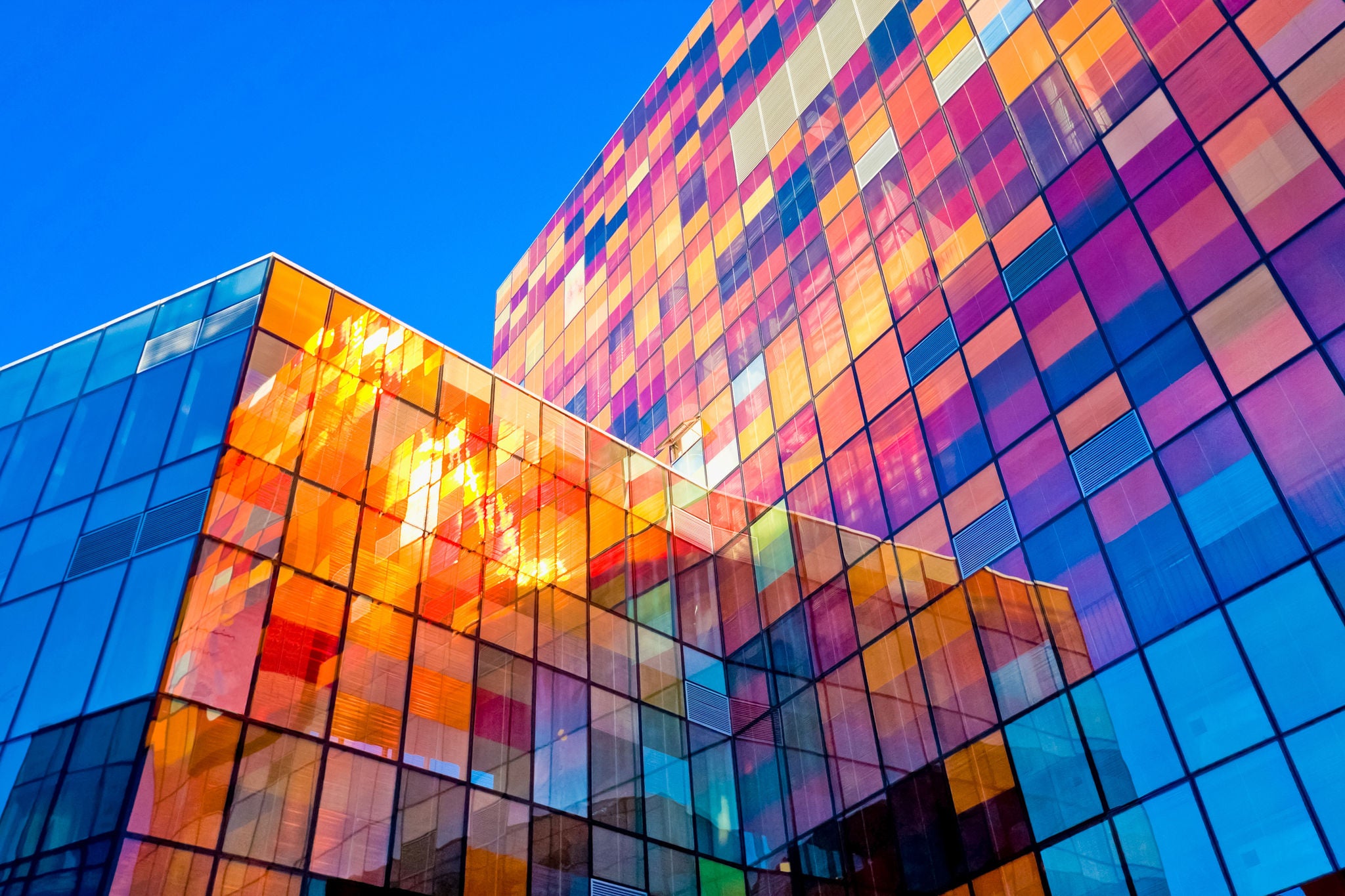 Farbenfrohe Glasfassade eines Bürogebäudes mit geometrischen Mustern und Sonnenr