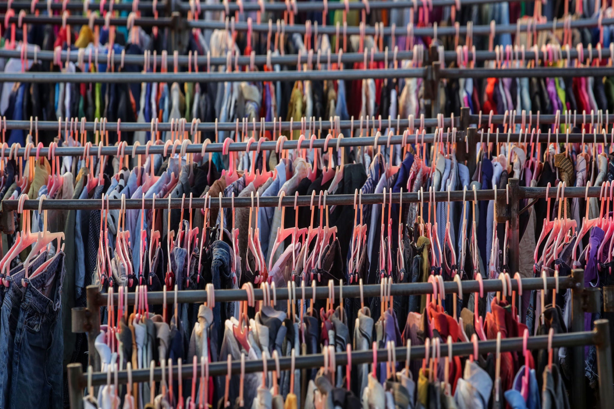 Huge selection of different used clothes for men, women and children on the rack in a second hand shop or thrift store. Concept of waste problem in fashion industry. 