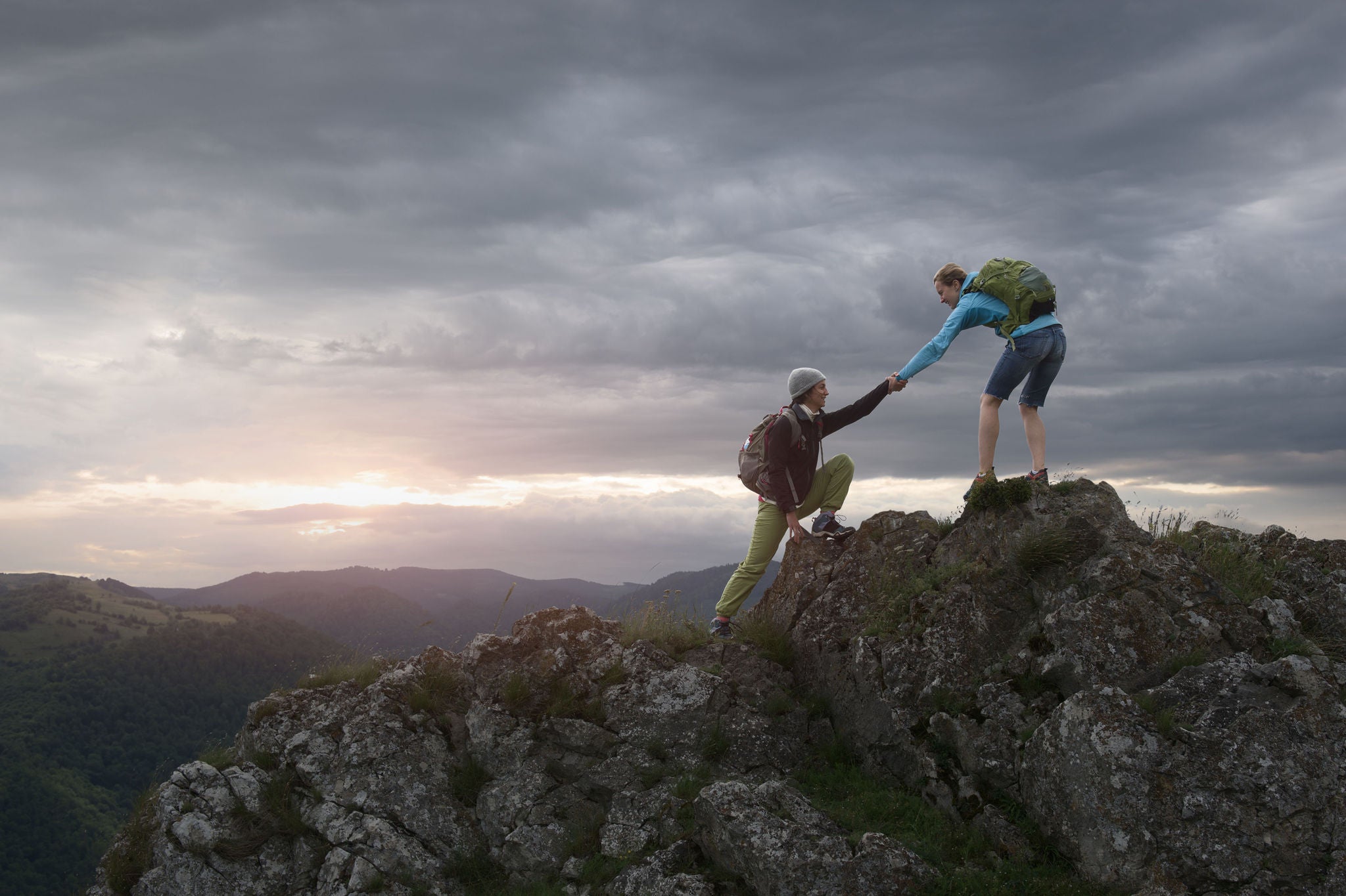 Hiker Woman helping her friend reach the top of the mountain