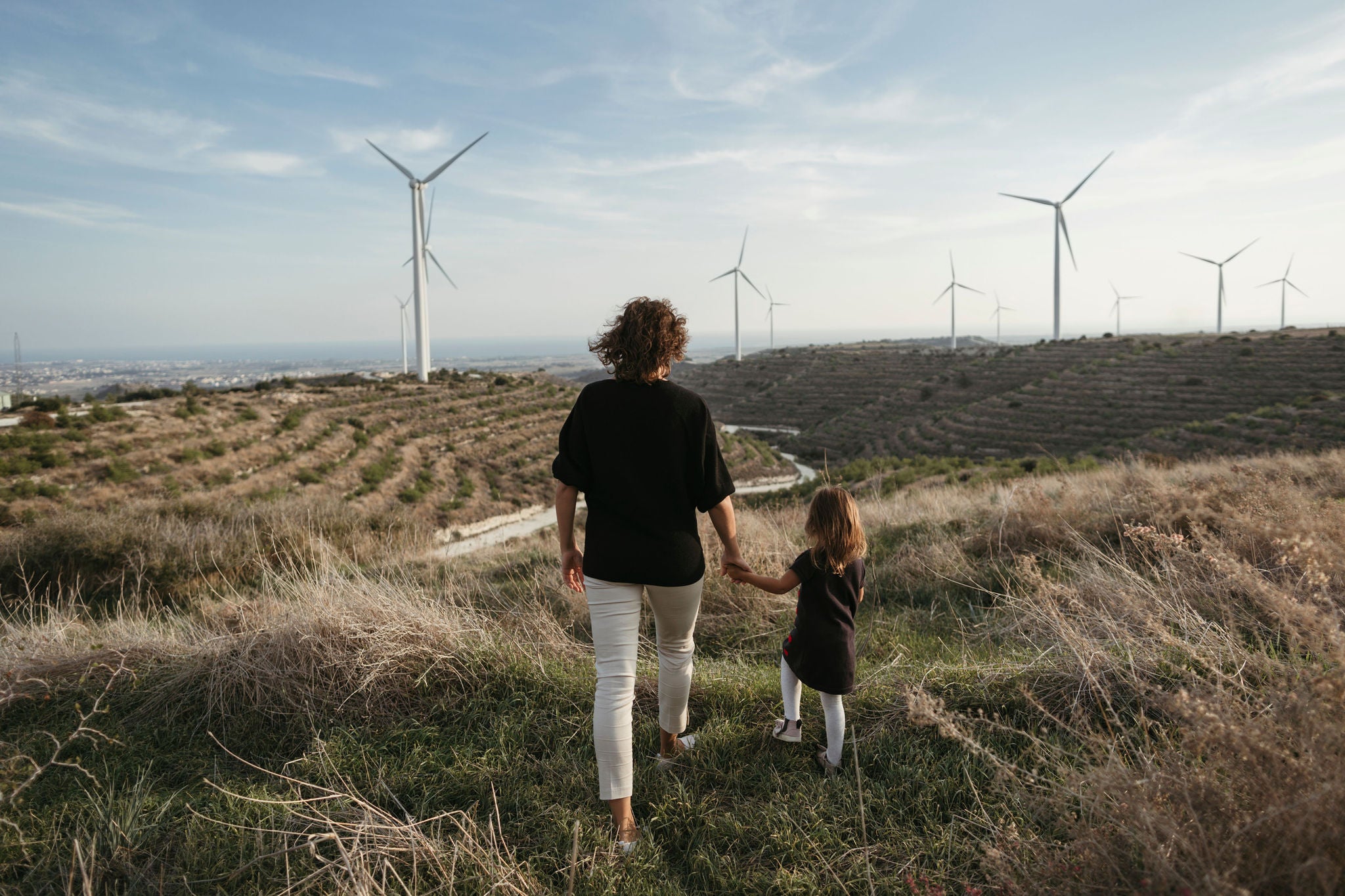 An anonymous mother with a small daughter walking in nature. Rocky landscape and windmills in the background.