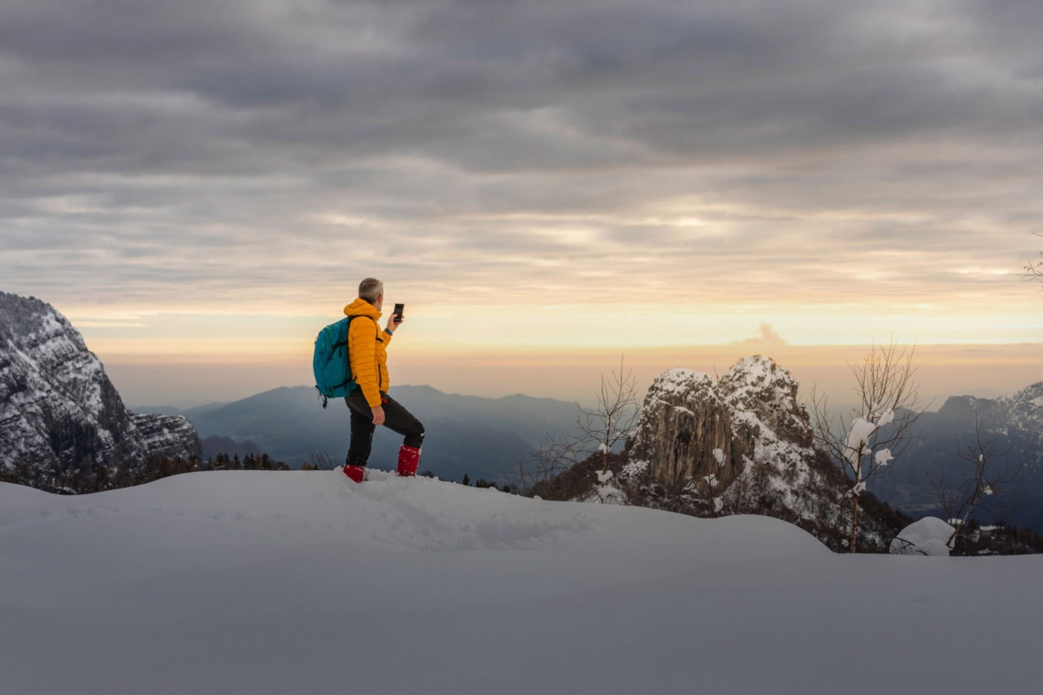 EY Alpinista tirando foto com smartphone ao nascer do sol na montanha nevada