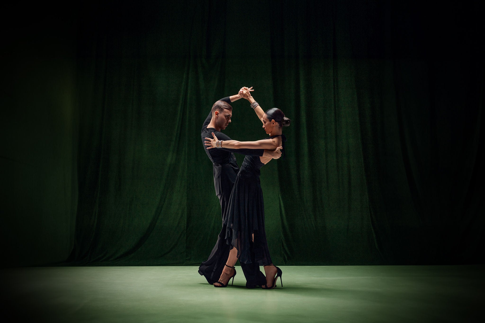 Ein Paar, professionelle Tango-Taenzer, in schwarzen Buehnenkostuemen vor dunkelgruenem Hintergrund