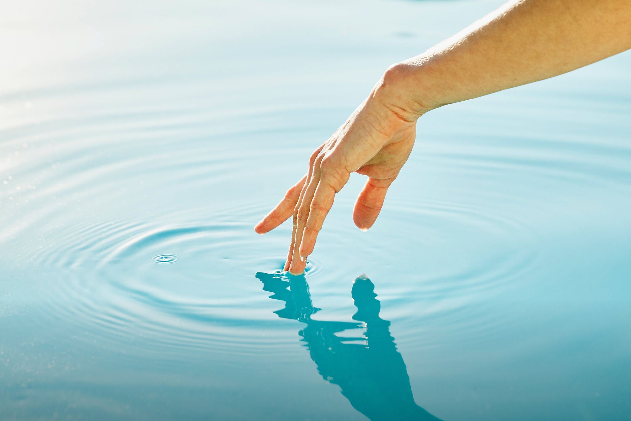 Hand delicately dipping fingertips into a pool of clear tranquil water