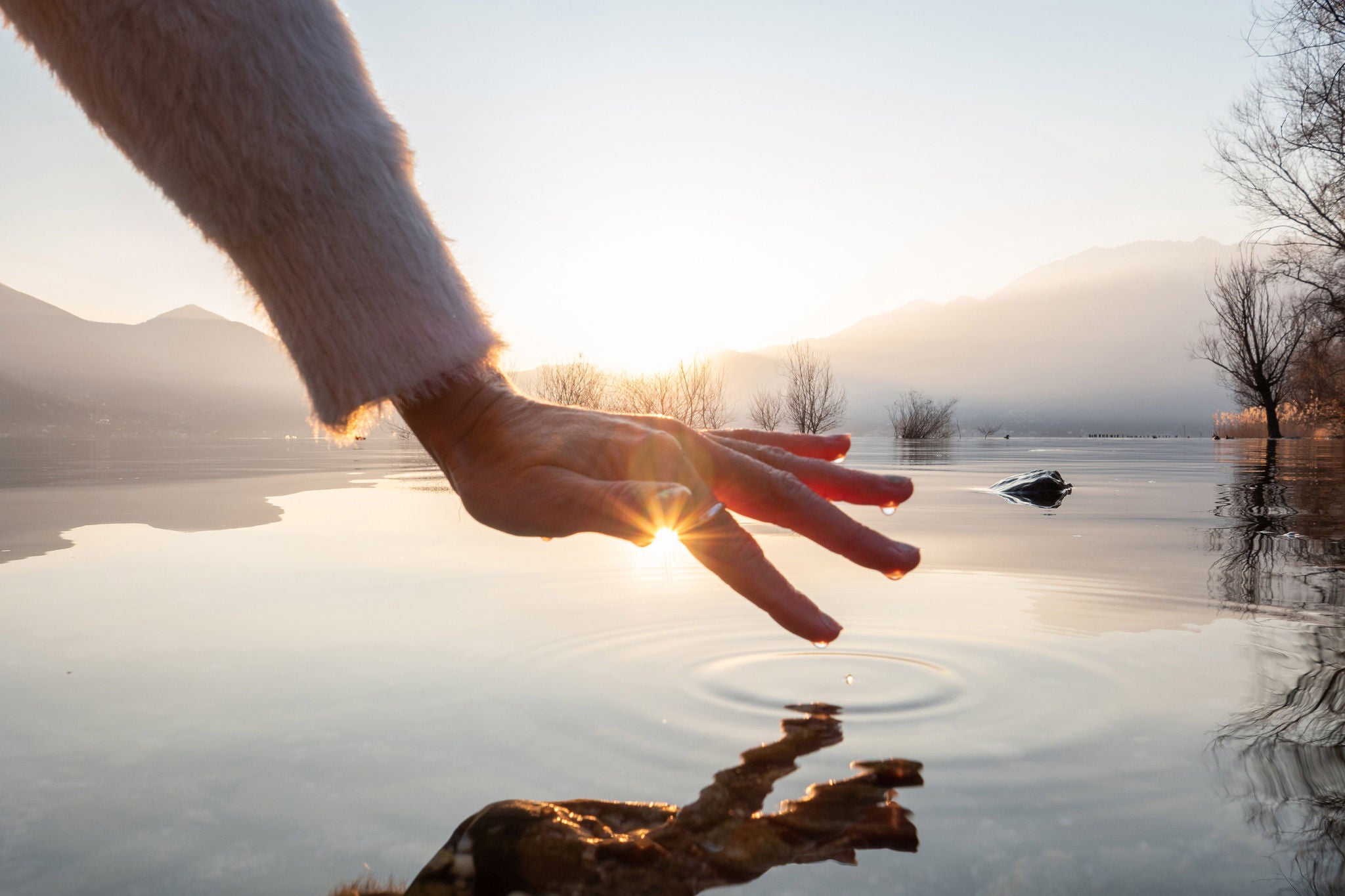 Detail of hand touching water surface of lake at sunset