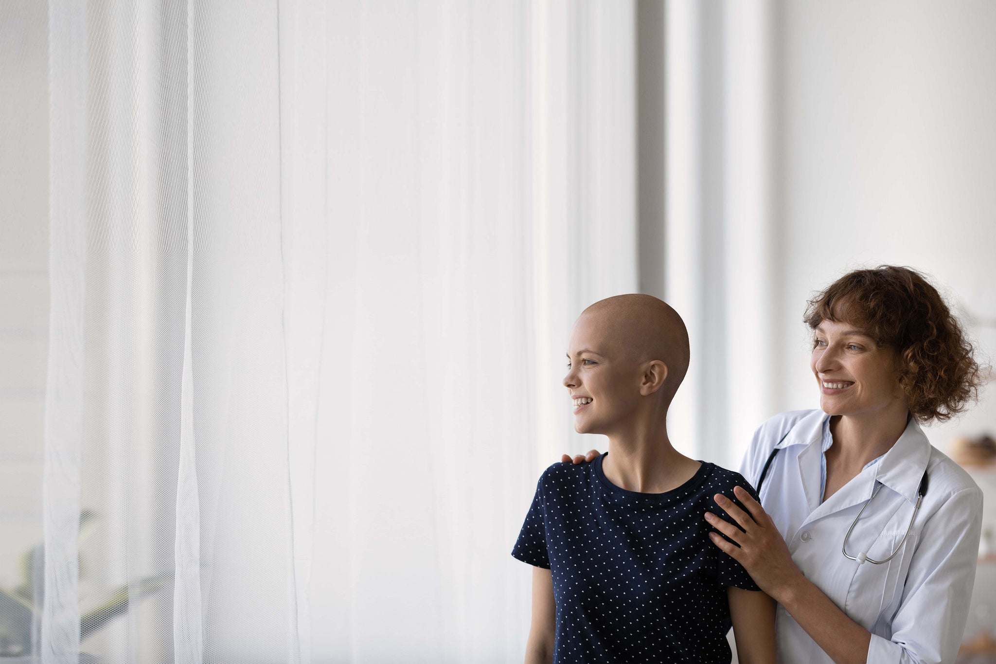 Smiling Caucasian doctor or nurse support comfort millennial woman struggle with oncology. Happy GP and optimistic female cancer patient look in distance dream of illness recovery or remission.