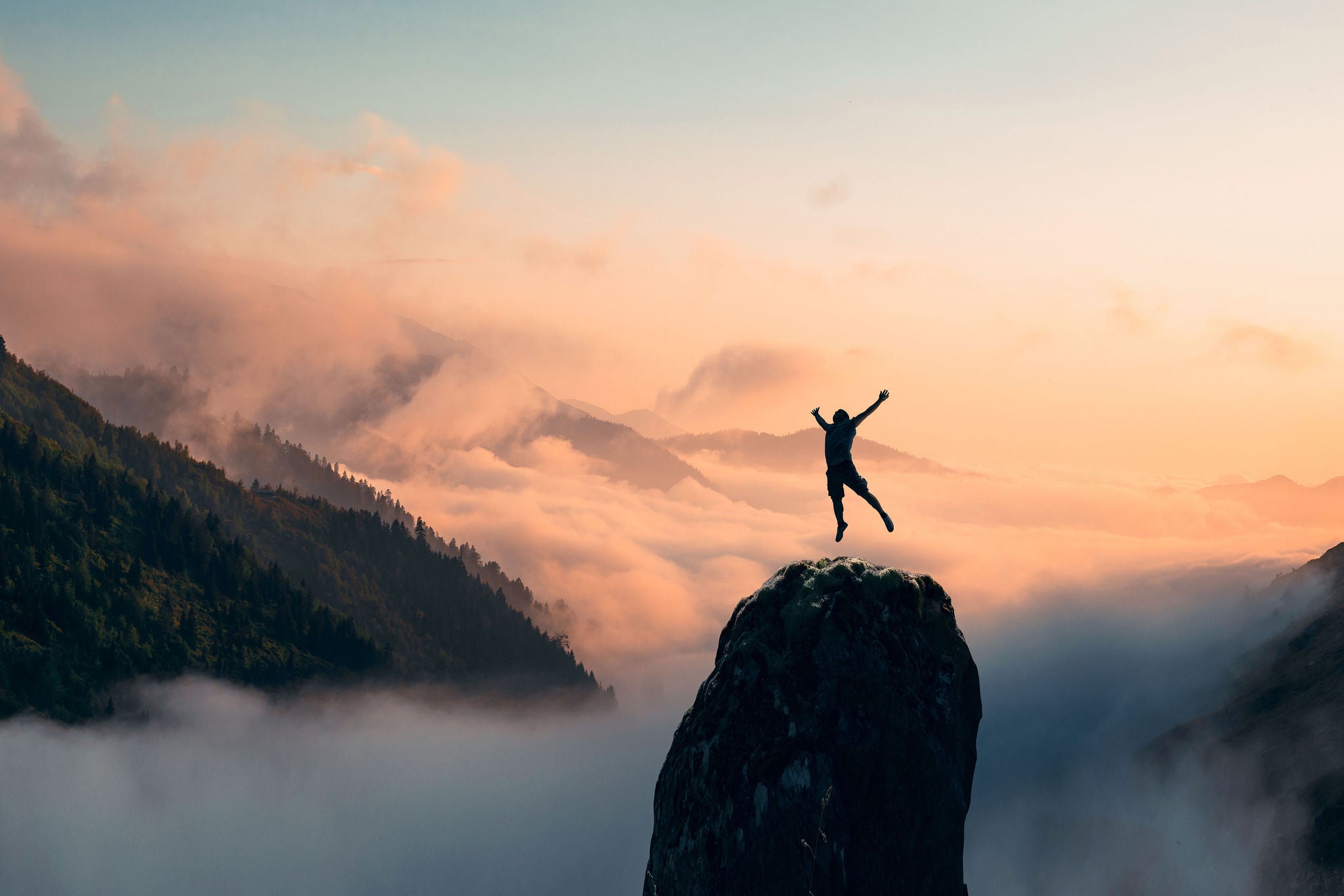 Silhouette of a Man jump and rises arms up on a peak. The happiness and excitement of beeing successful. High quality photo