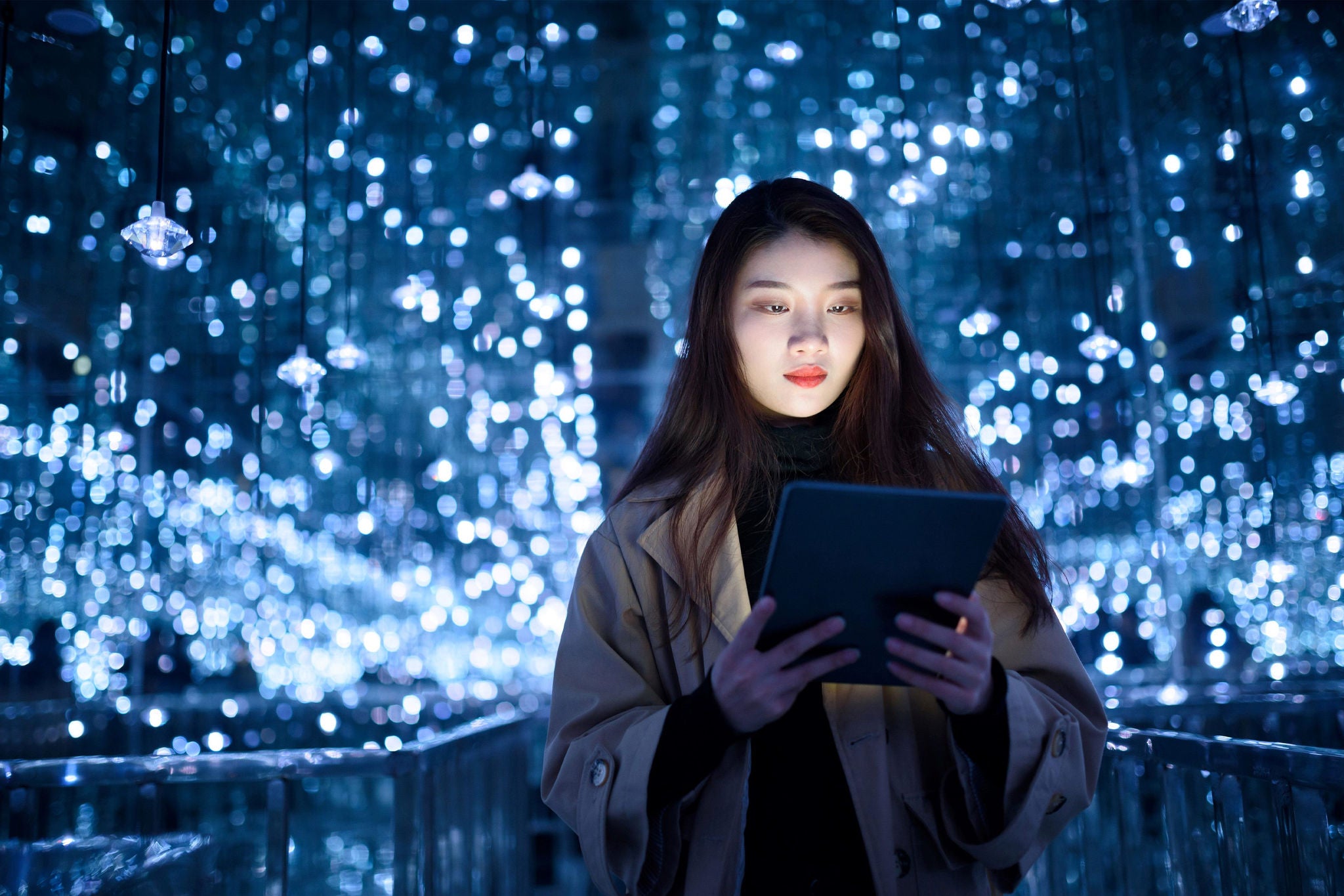 Young woman reading a tablet amid a display of blue hanging lights