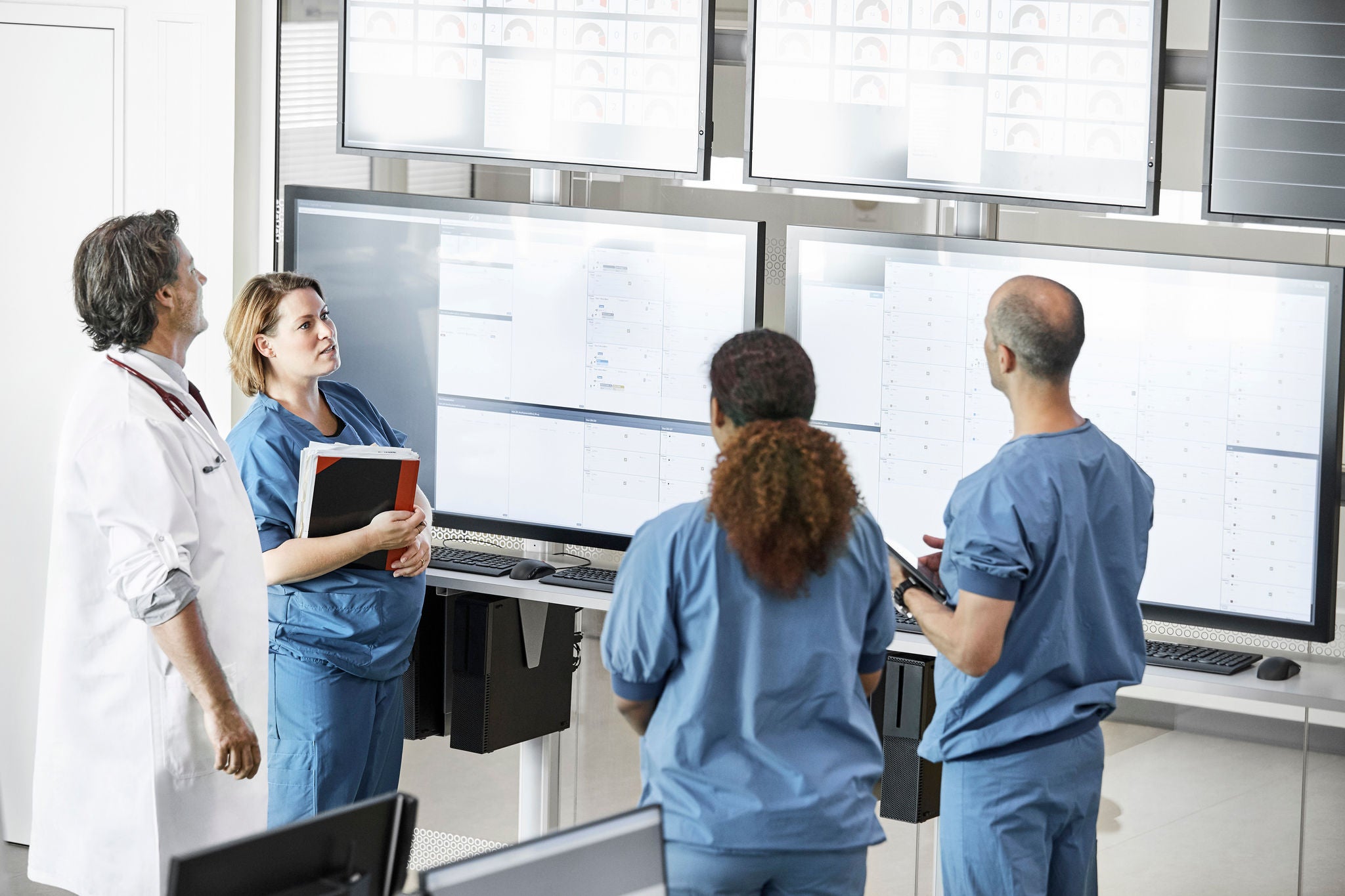 High angle view of male and female healthcare workers discussing over screens. Medical professionals are communicating in meeting at control room. They are planning strategy at medical center.