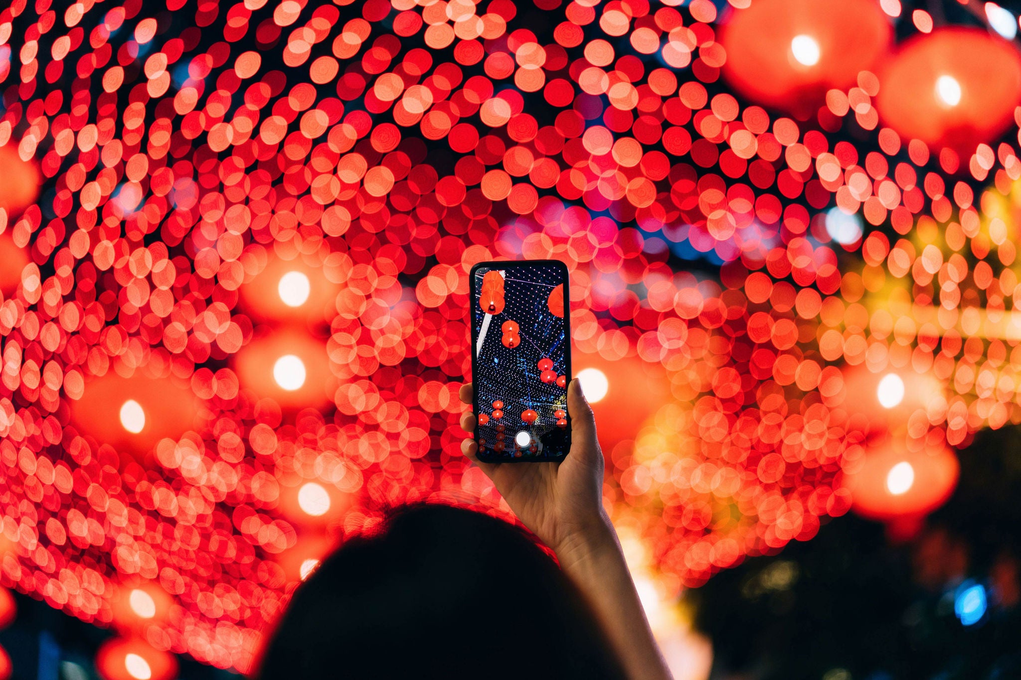 Asian woman taking photos of illuminated traditional Chinese red lanterns 