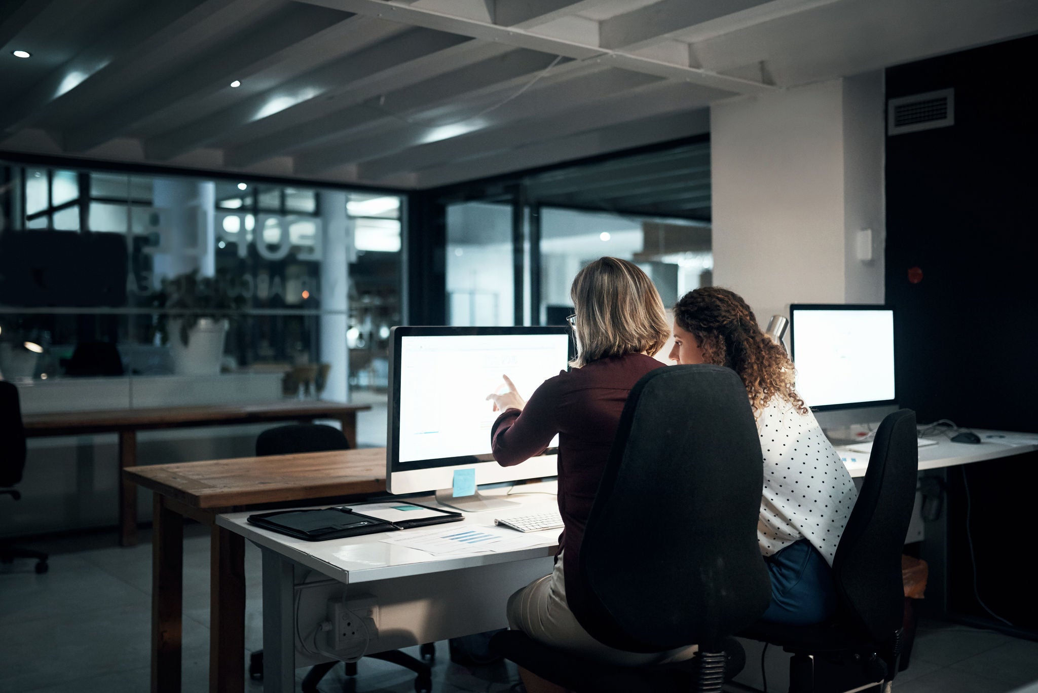 Two women discussing business report displayed on computer screen