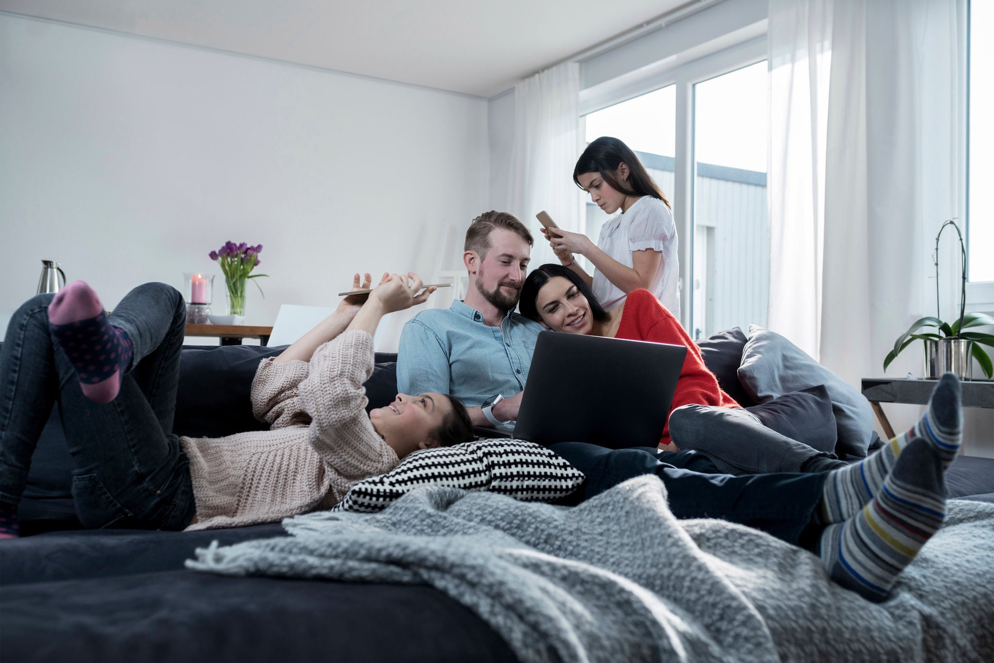 Image d'une famille joyeuse avec des visages souriants, réunie et utilisant divers gadgets électroniques.