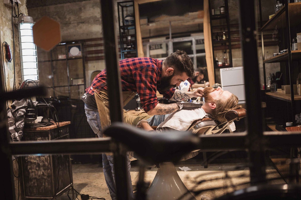 Barbier trimmt Bart eines bÃ¤rtigen Mannes im Barbershop