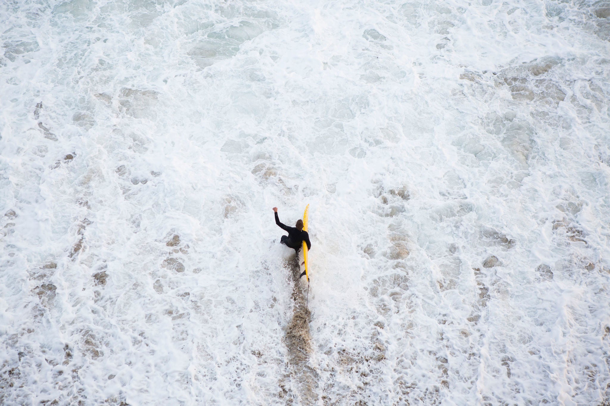 Surfer in black wet suit walking into turbulent waters carrying yellow surfboard, Surfer in black wet suit walking into turbulent waters carrying 