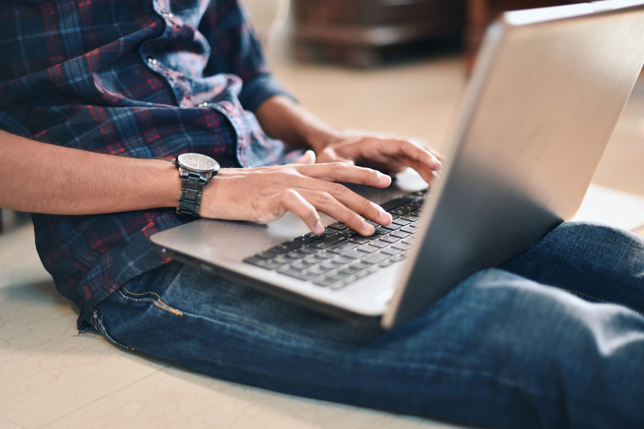 Un hombre sentado en el suelo con una notebook colocada sobre sus piernas, se encuentra tipeando en el teclado.