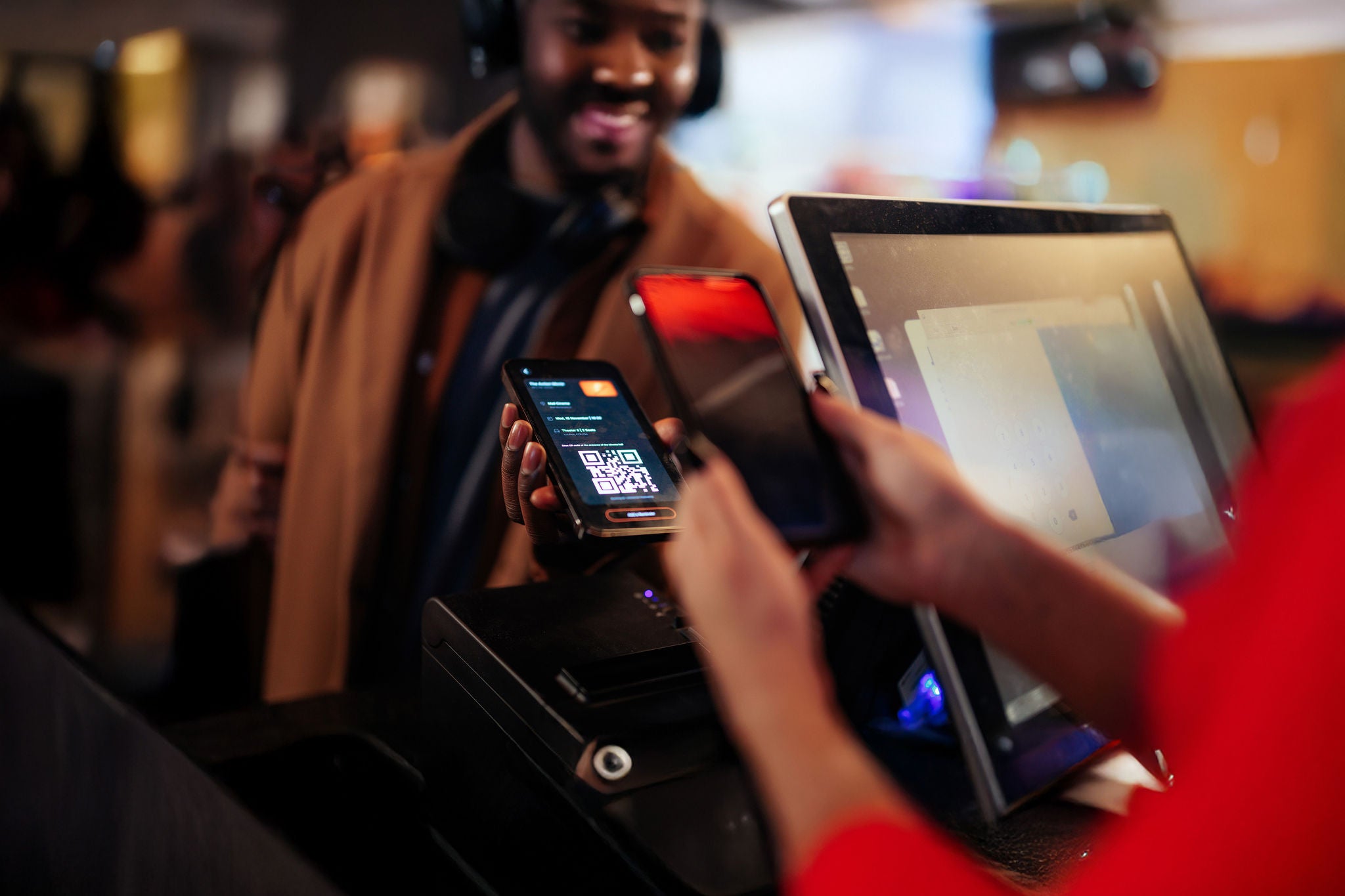 A man is paying contactless in a movie theater with his mobile phone app while the cashier is scanning his app at the register.