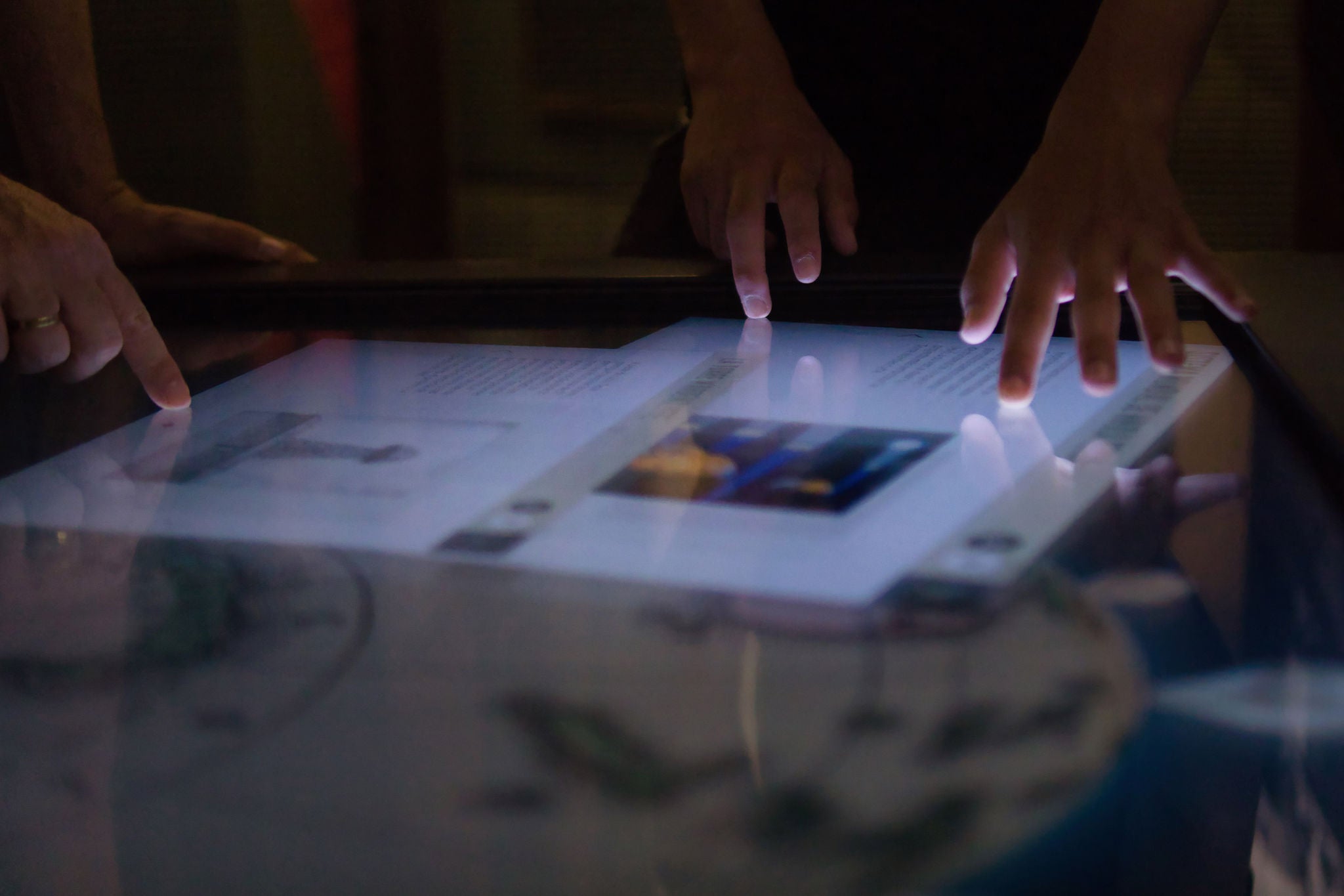 Three different hands touch a large interactive screen that glows from within