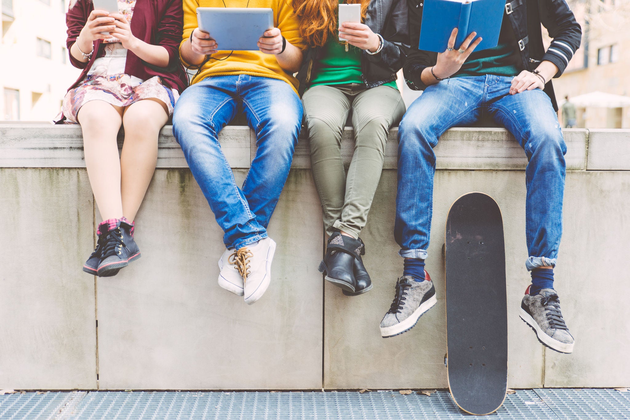 Group of teenagers making different activities sitting in an urban area