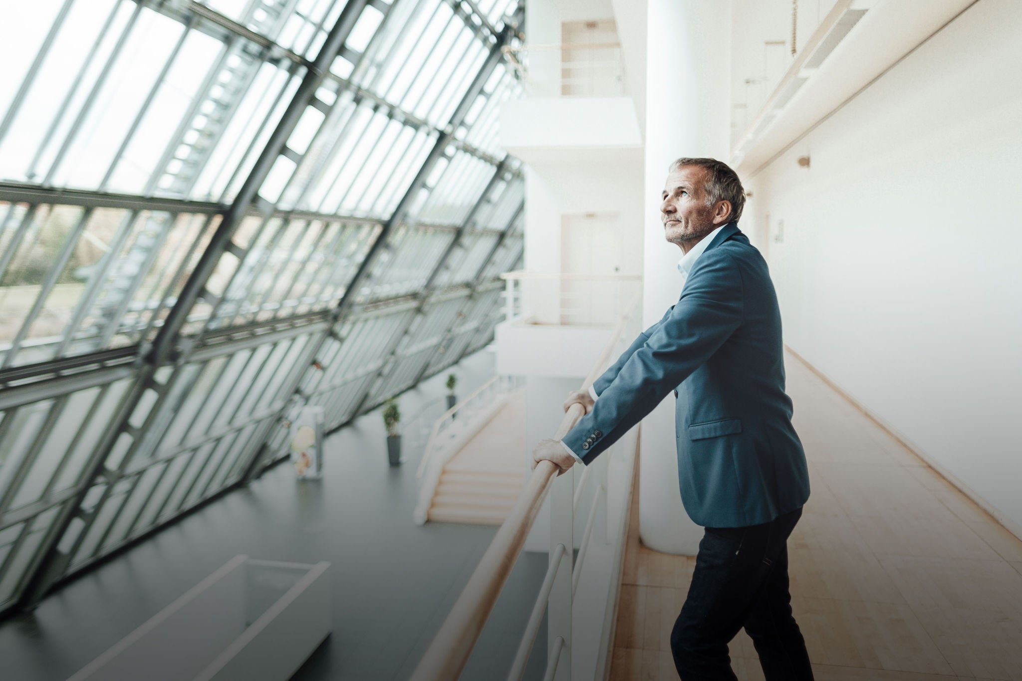 Thoughtful businessman looking away while leaning on railing in office corridor