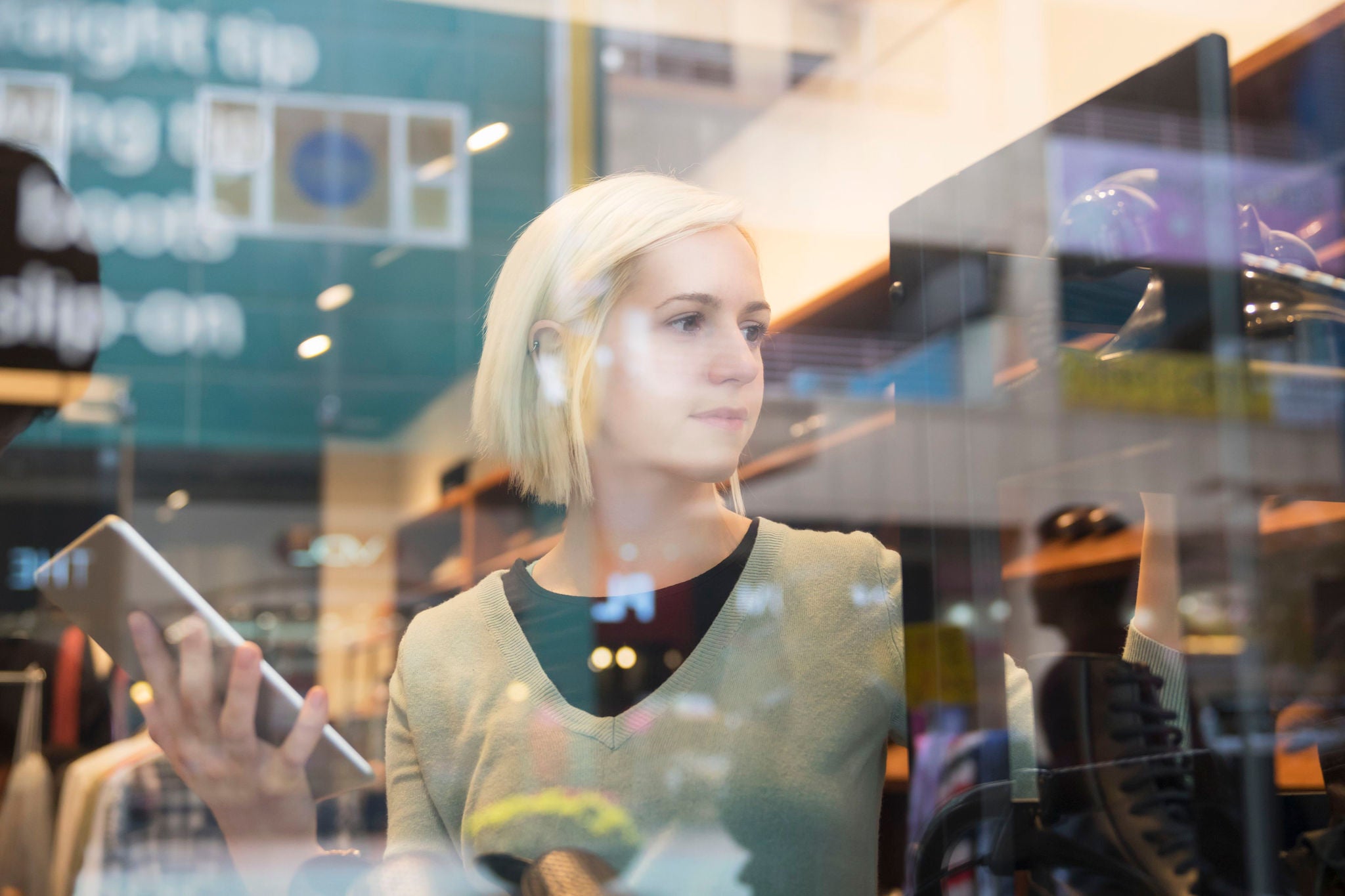 A girl with short hair holding a tablet viewed through a glass window