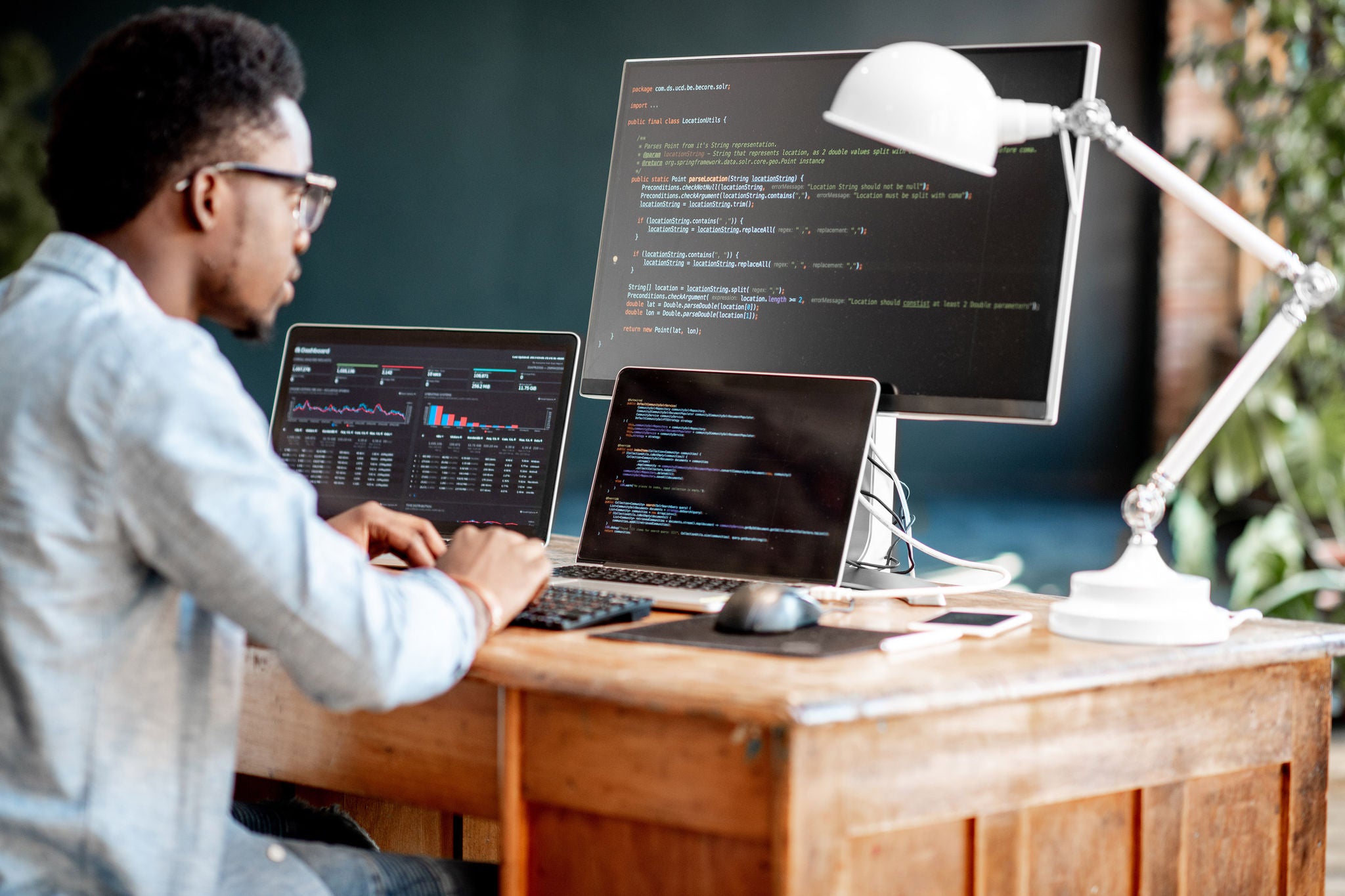 Young african male programmer writing program code sitting at the workplace