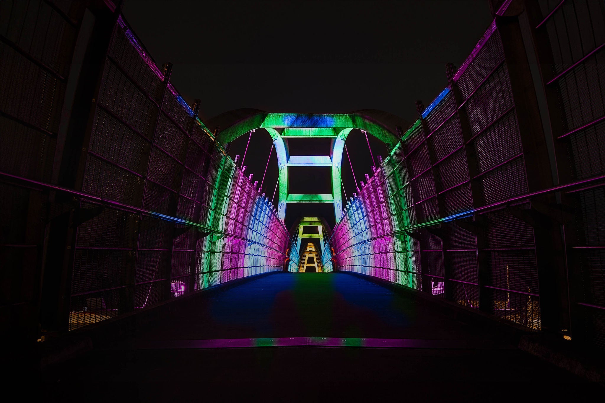 Bright colors illuminate pedestrian walkway over highway at night