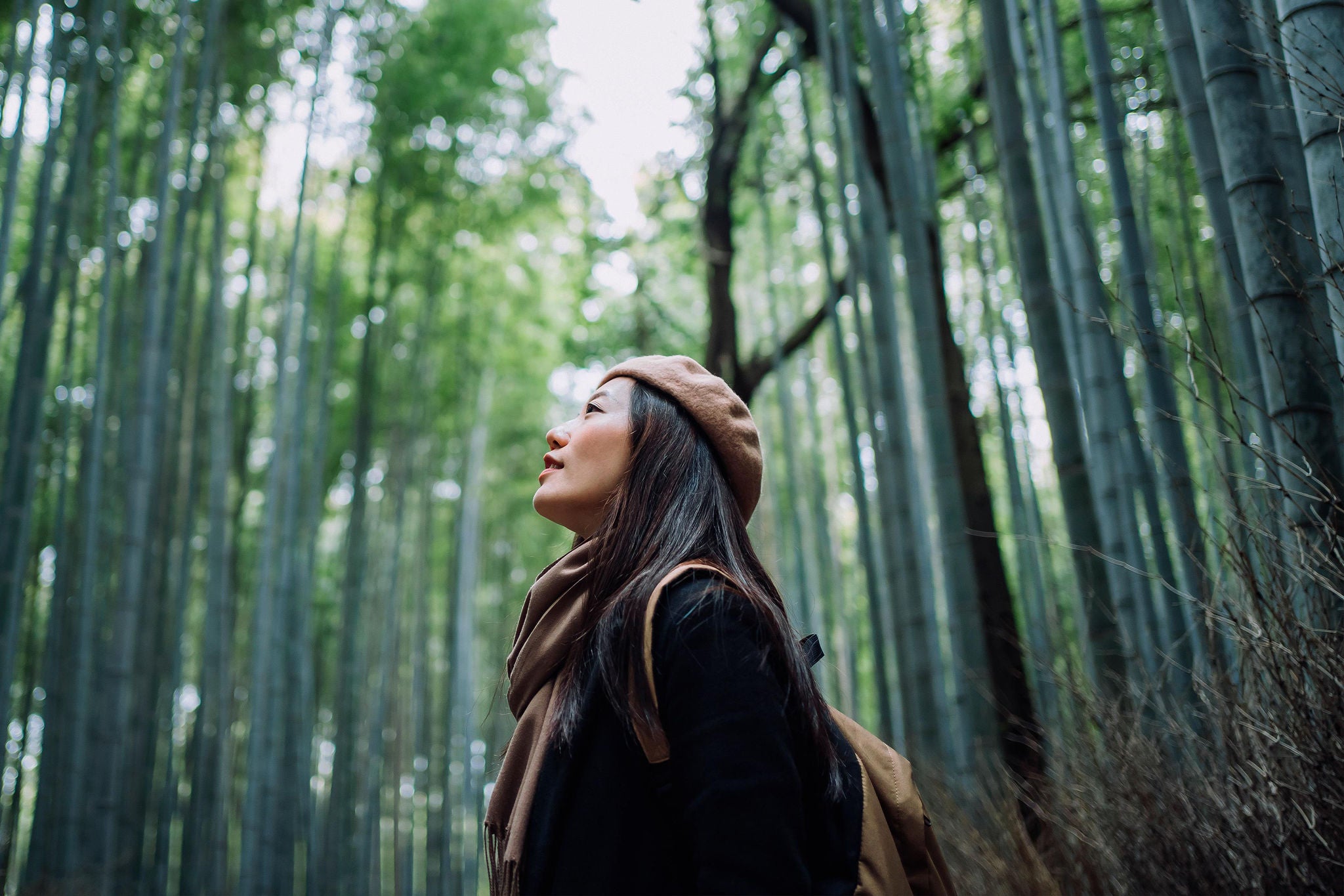 Young Asian female backpacker enjoying in nature. Taking a deep breath of fresh air while having a relaxing walk in the bamboo forest in the countryside during the outbreak of coronavirus pandemic