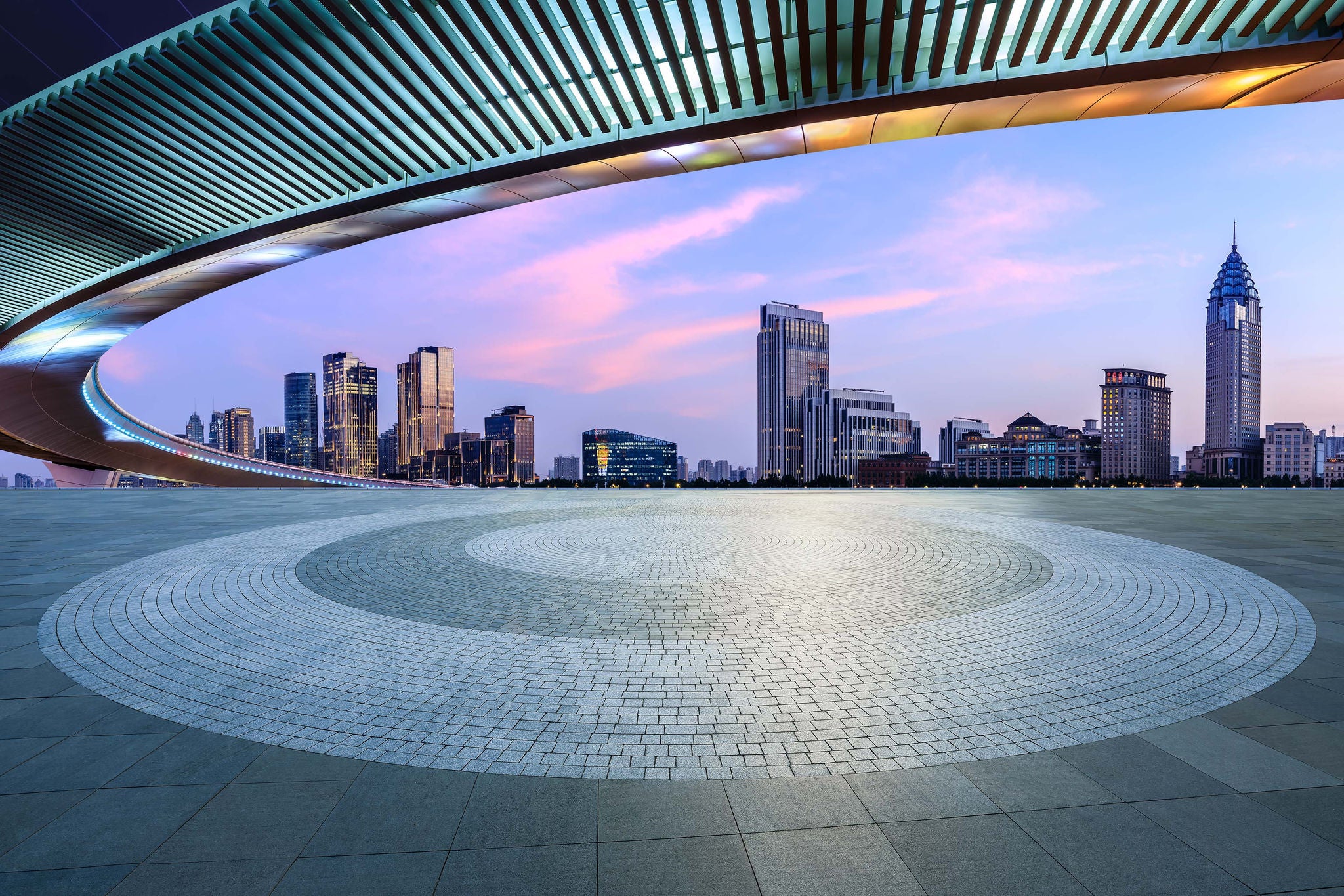 Round square floor and pedestrian bridge with modern city buildings at dusk in Shanghai