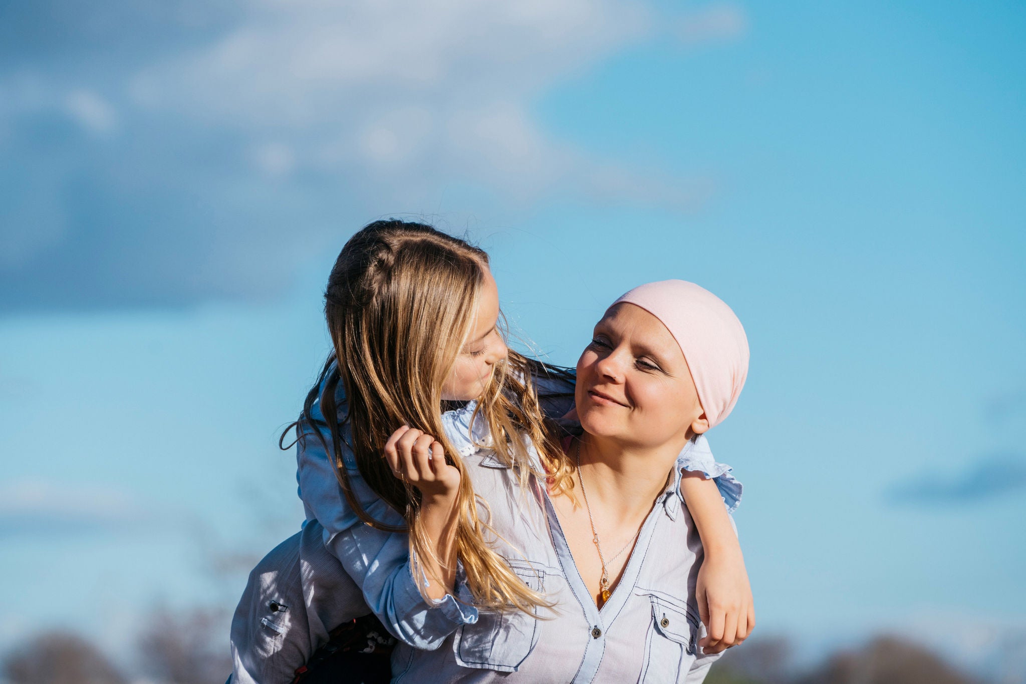 A woman with cancer is next to her daughter. A girl is hugging a woman happy 
