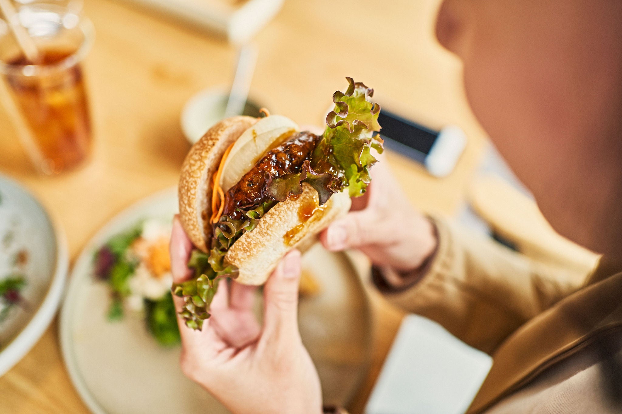 Asian woman enjoying vegan hamburger and iced tea lunch at a vegan cafe.