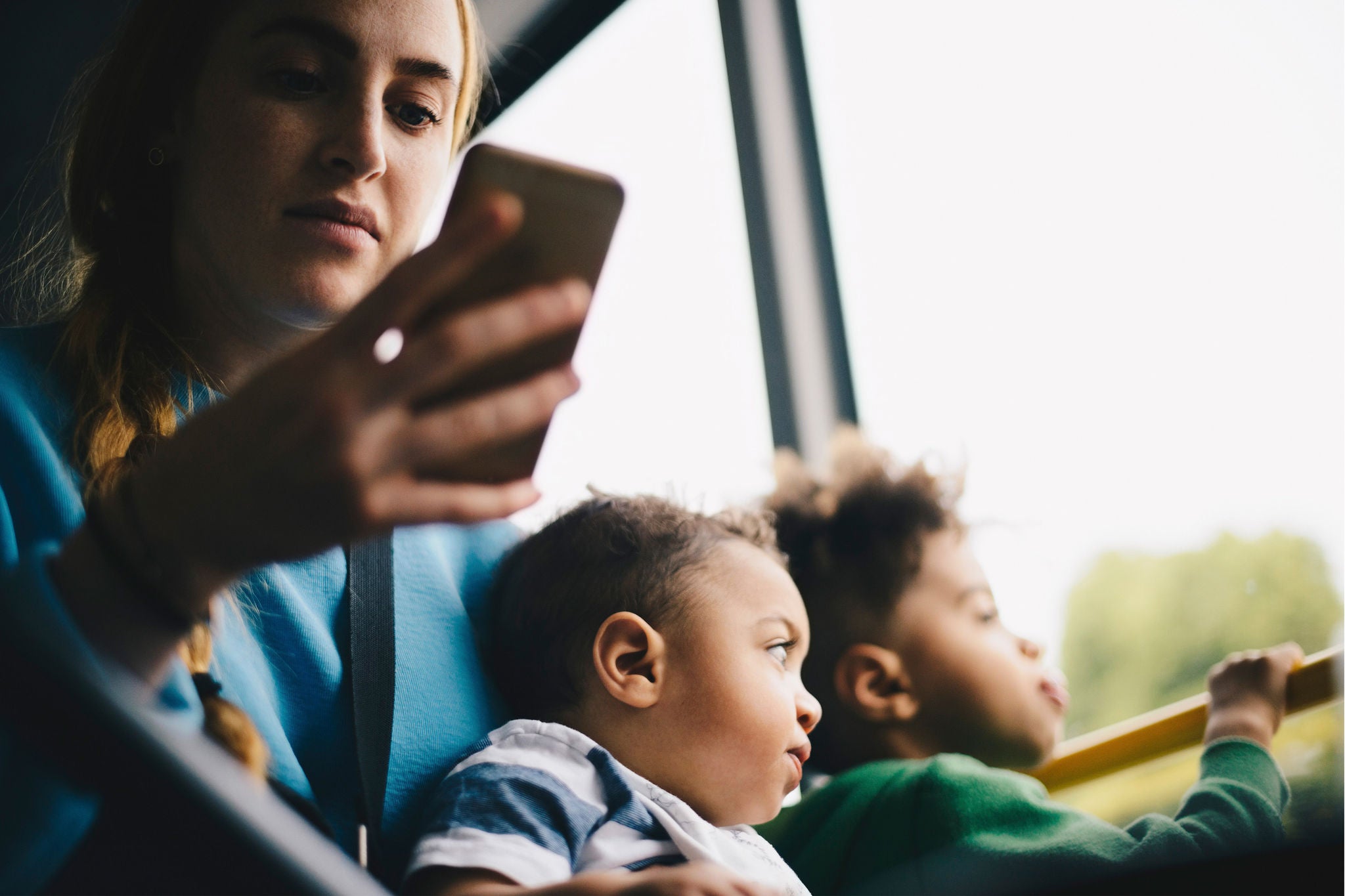 Mother using mobile making her kid sit on her lap