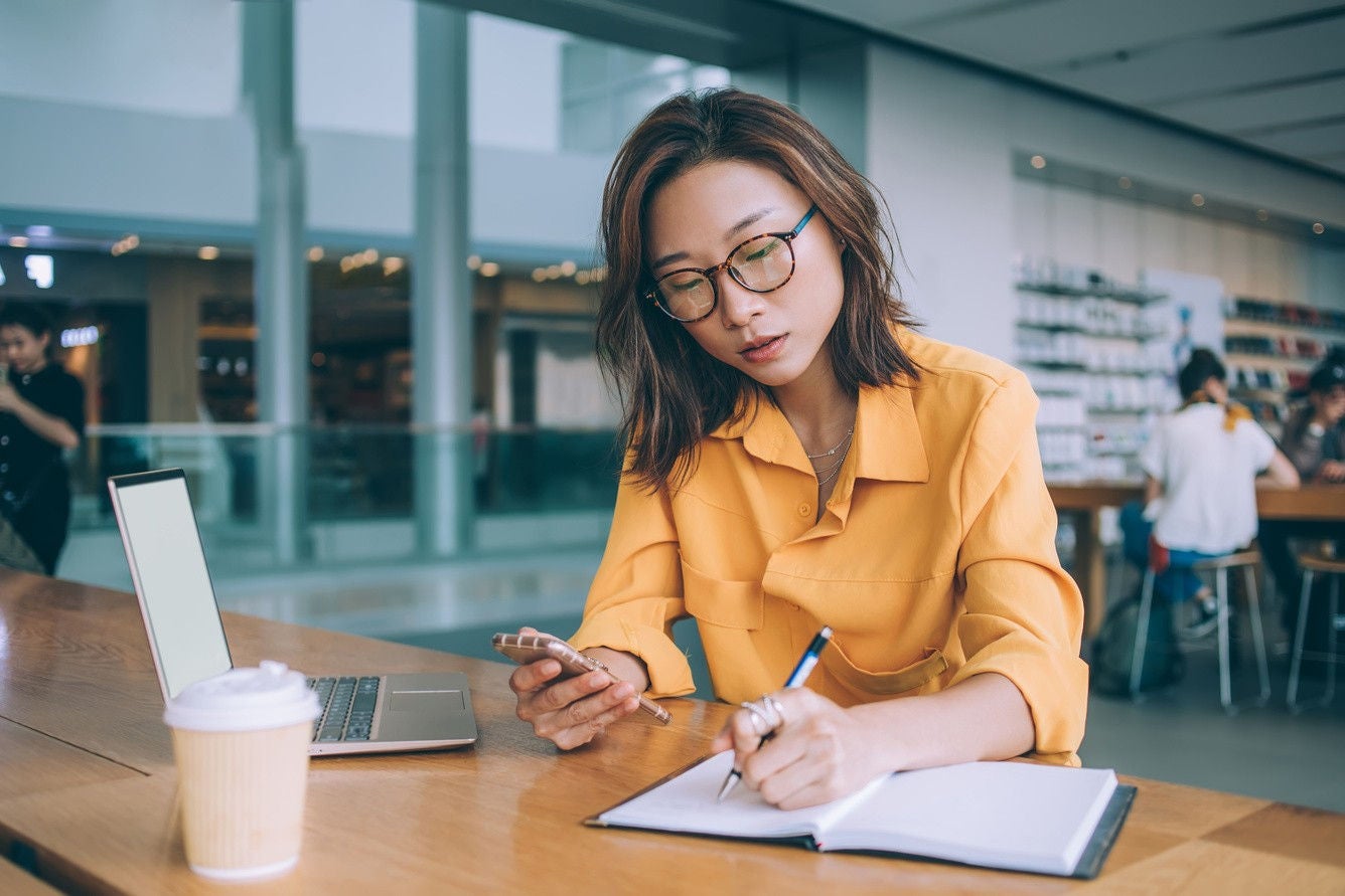 A woman writing notes while browsing in the mobile