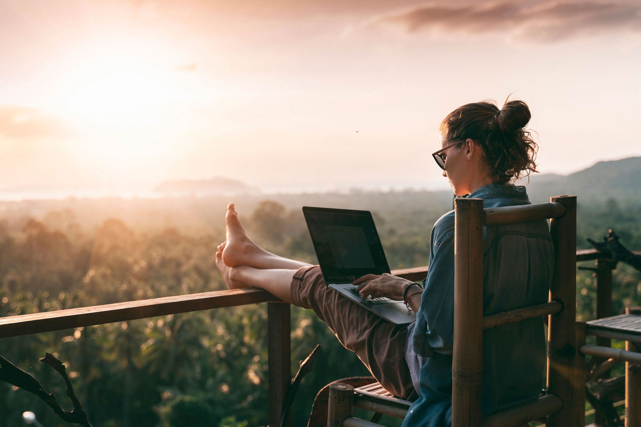 Young business woman working at the computer in cafe on the rock. Young girl downshifter working at a laptop at sunset or sunrise on the top of the mountain to the sea, working day.