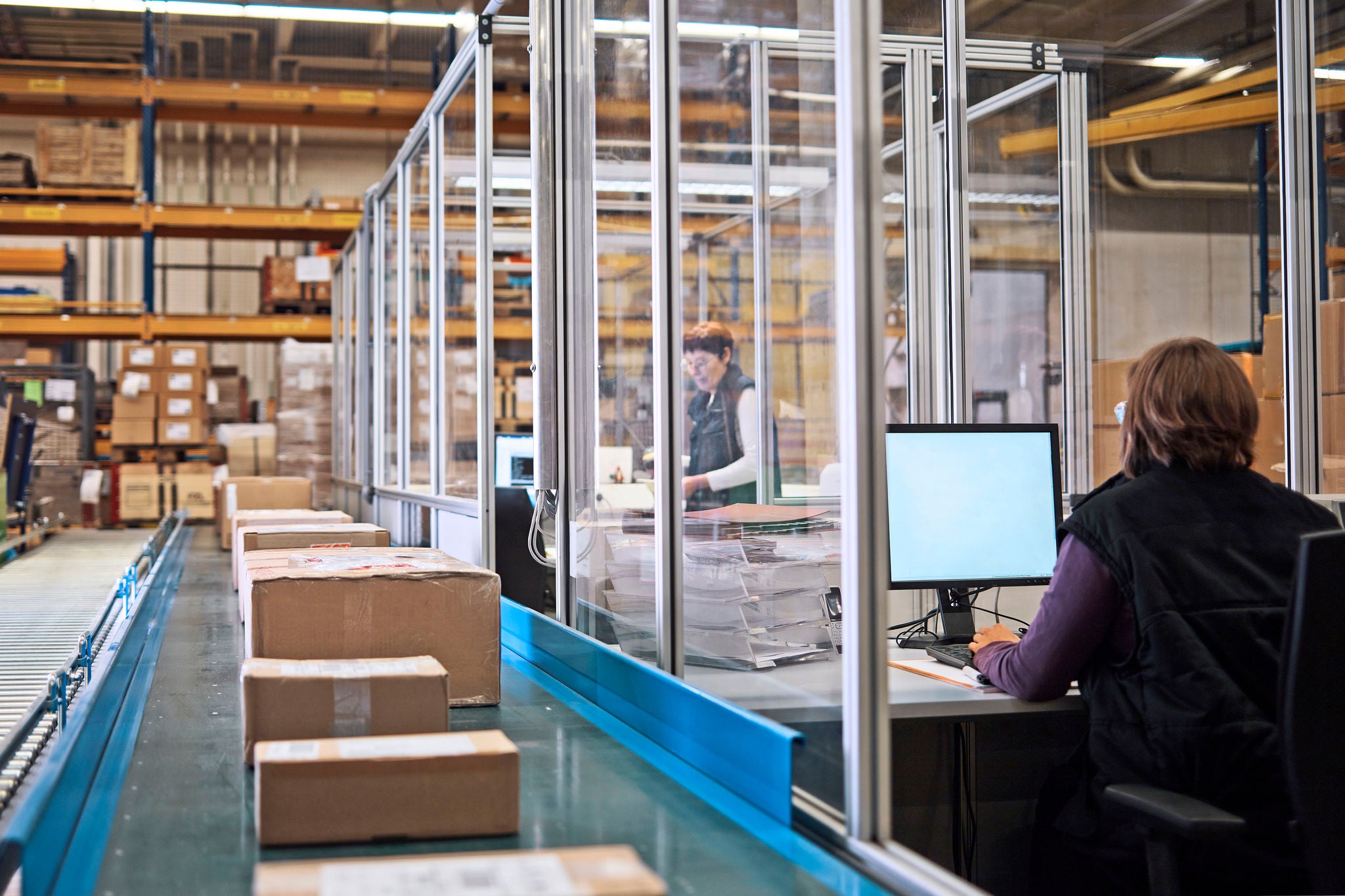 Two women in storehouse with packages on conveyor belt