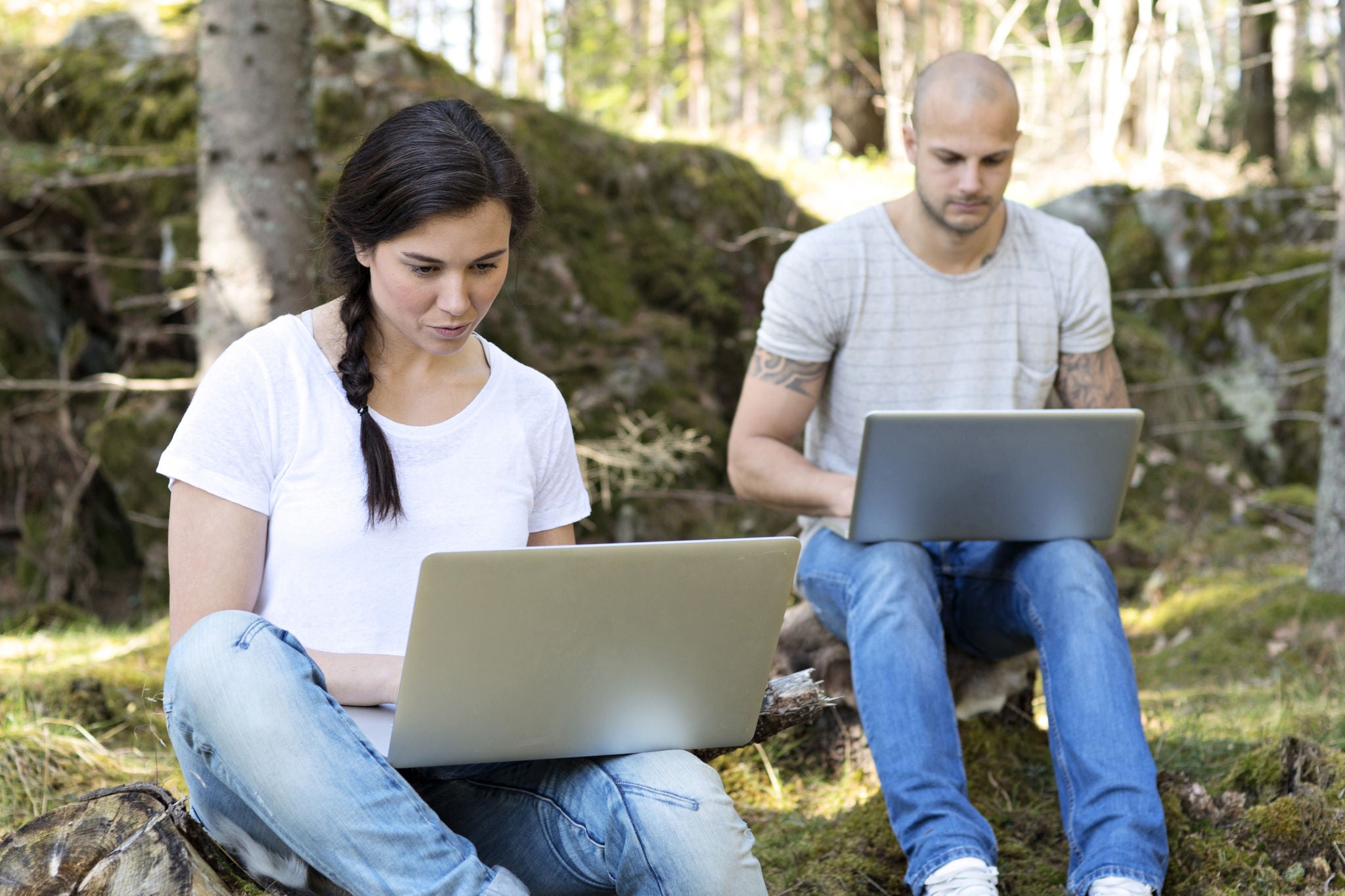 Man and woman sitting with laptops outdoors, looking at the screen