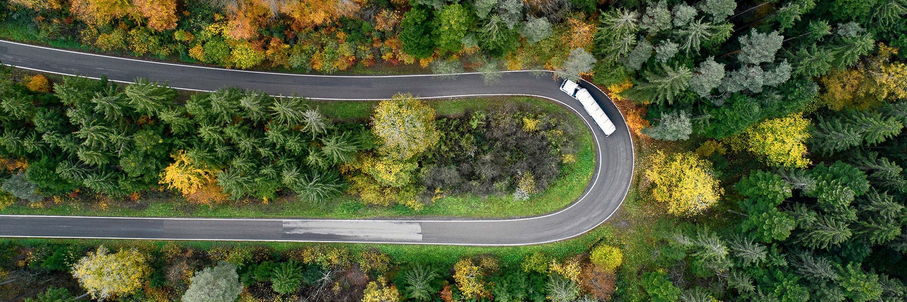 Aerial view of a winding road cutting through a forest filled with green, yellow, and orange autumn foliage