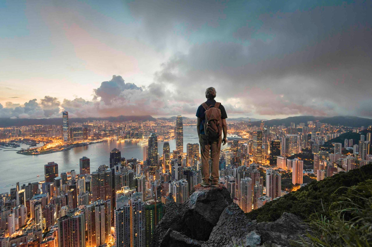 A man standing on a rock overlooking hong kong skyline at dawn from victoria peak