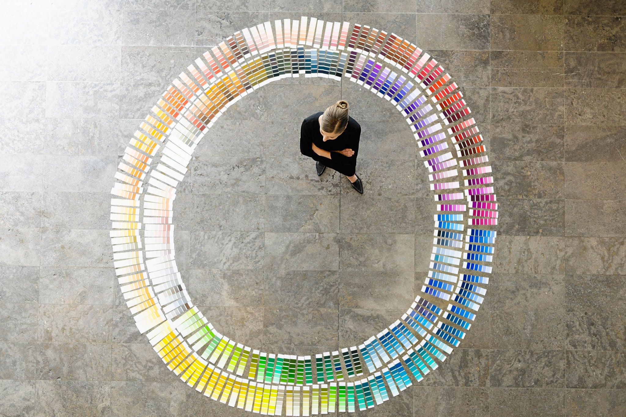 An overhead view of a person standing in the center of a large circular arrangement of color swatches spread out on the ground