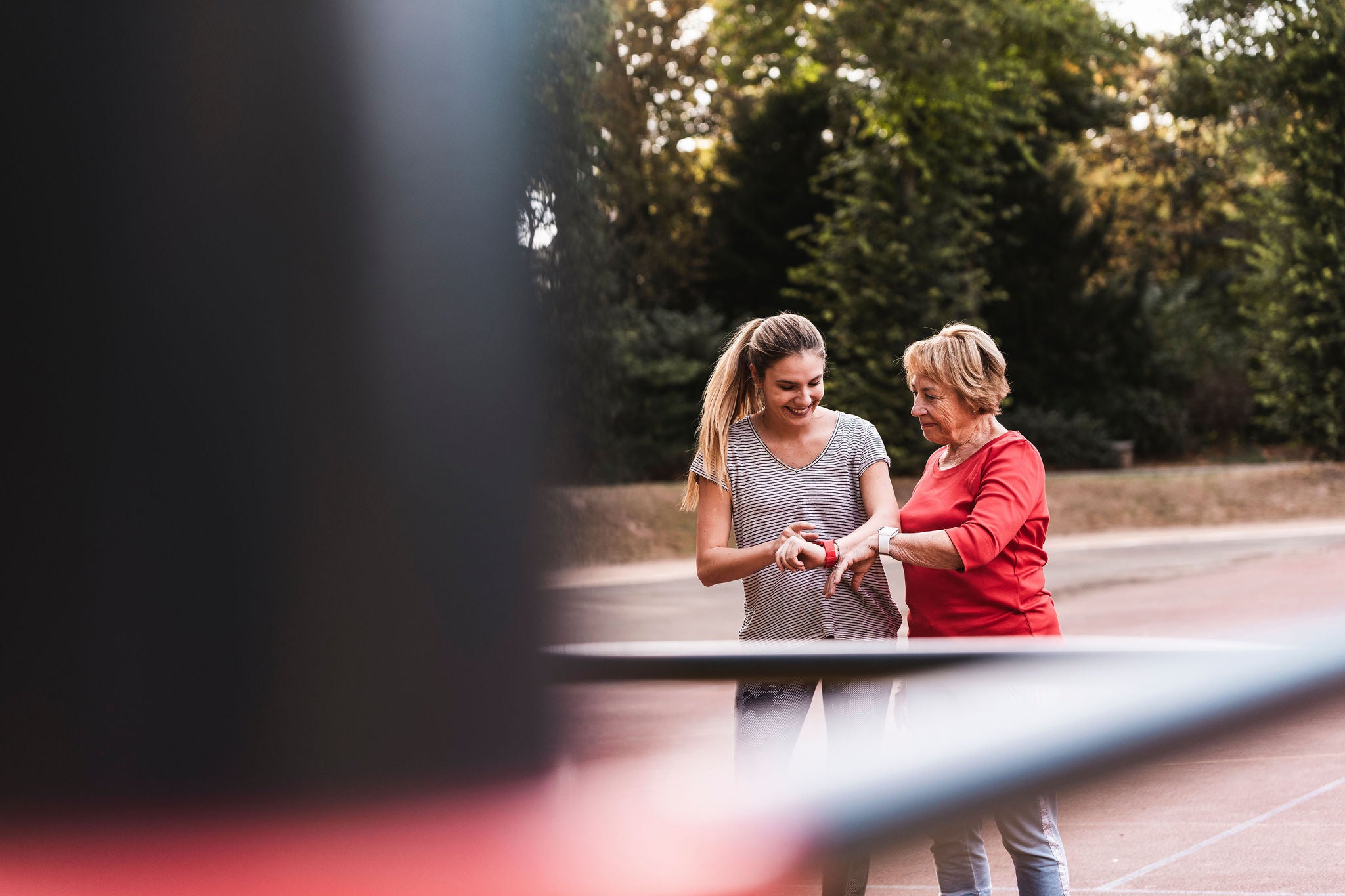 Happy woman examining fitness tracker with grandmother in park