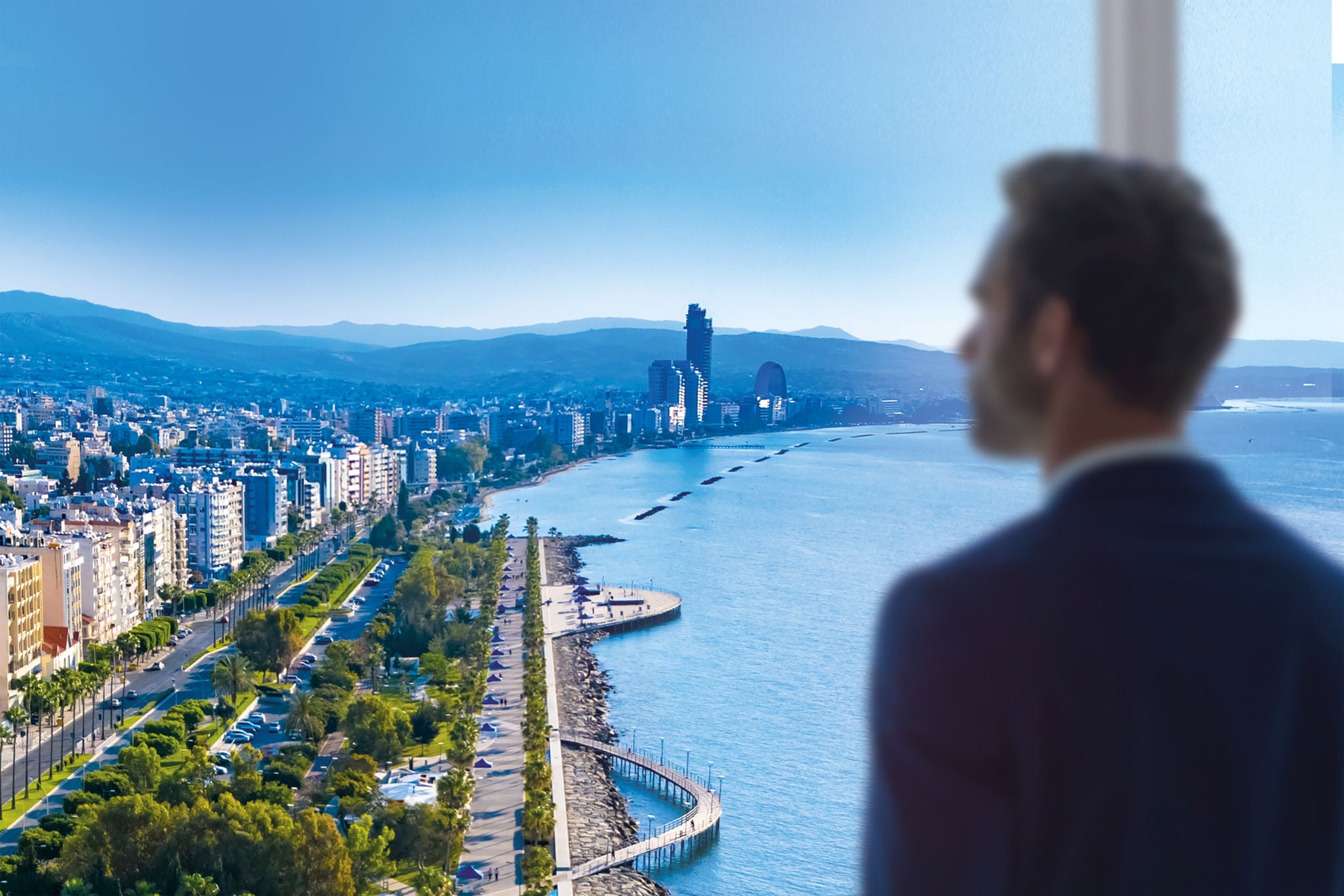 Man in a high rise building by the coast looking at cityscape 