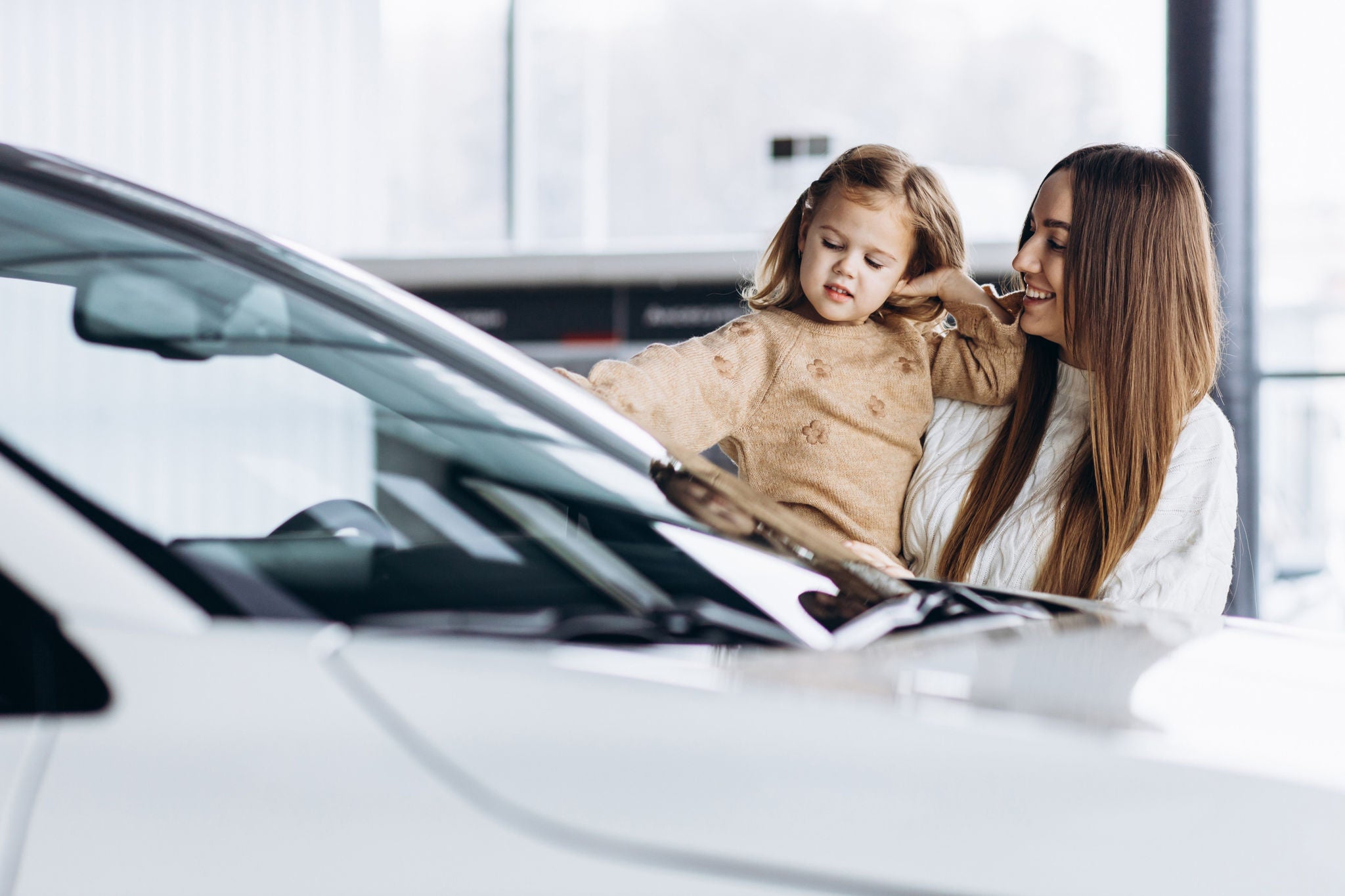 Mother with her little daughter choosing a car in a car showroom