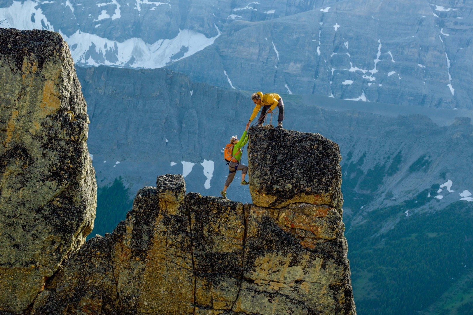 mountaineers scale rocks steps on cliff with rope